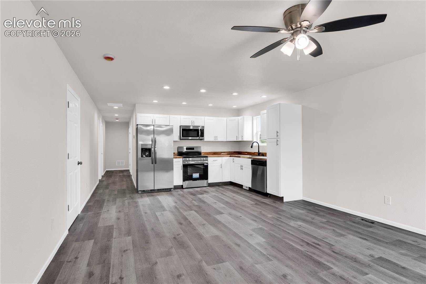 Kitchen featuring white shaker-style cabinetry, stainless steel appliances, wood-finish flooring, recessed lighting, and a ceiling fan
