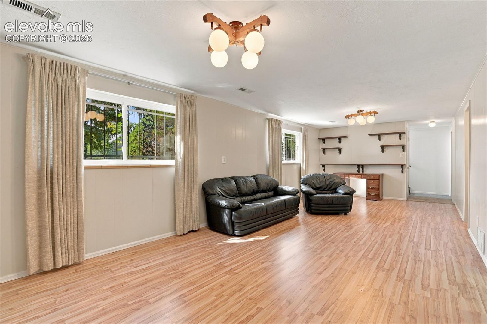 Expansive room featuring wood-finish flooring, two multi-globe semi-flush mount light fixtures, and wall-mounted shelving units