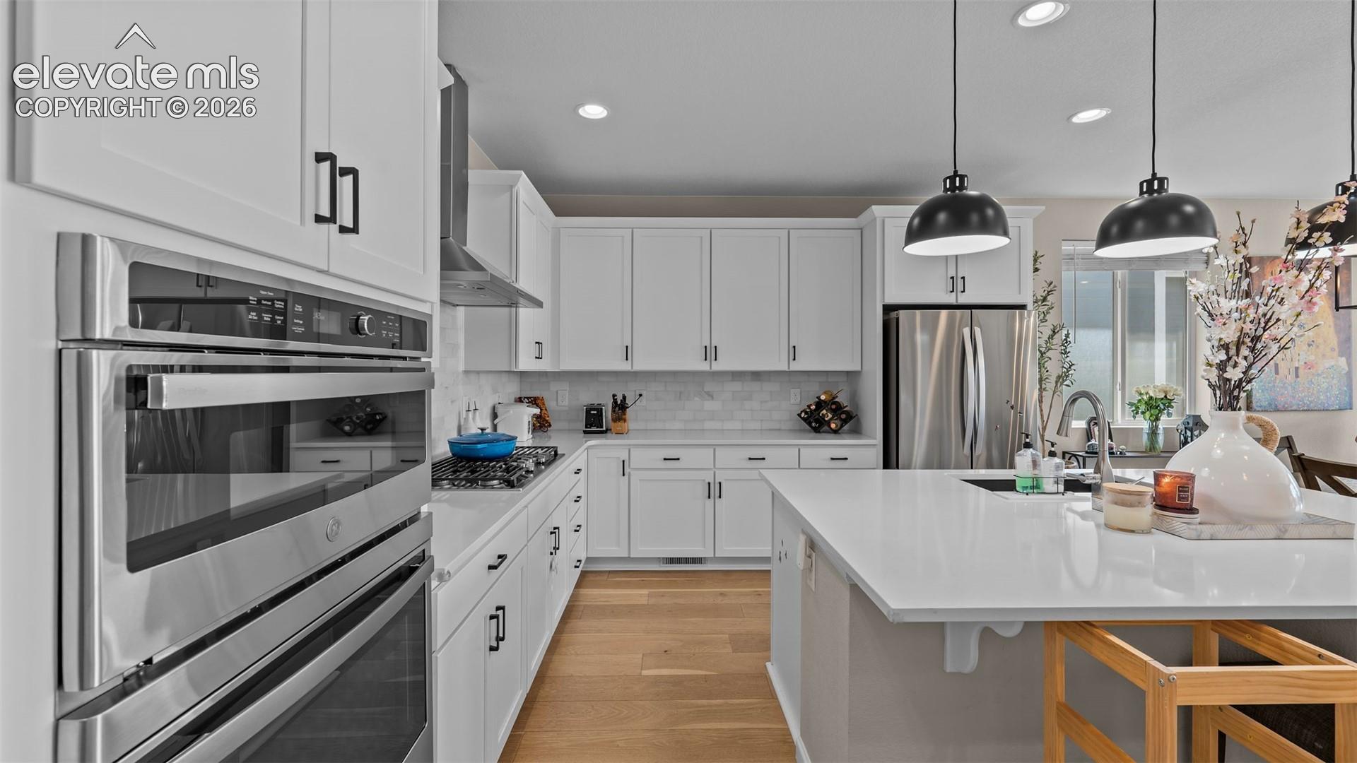 Kitchen featuring white cabinetry, stainless steel appliances, wood-finish flooring, a kitchen island, and pendant lighting