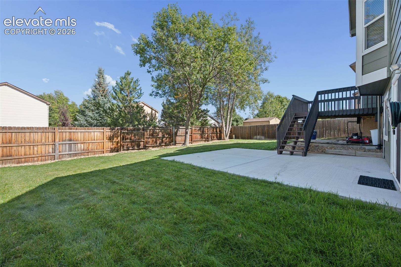 Backyard featuring a concrete patio, elevated wooden deck, wood privacy fencing, and mature trees