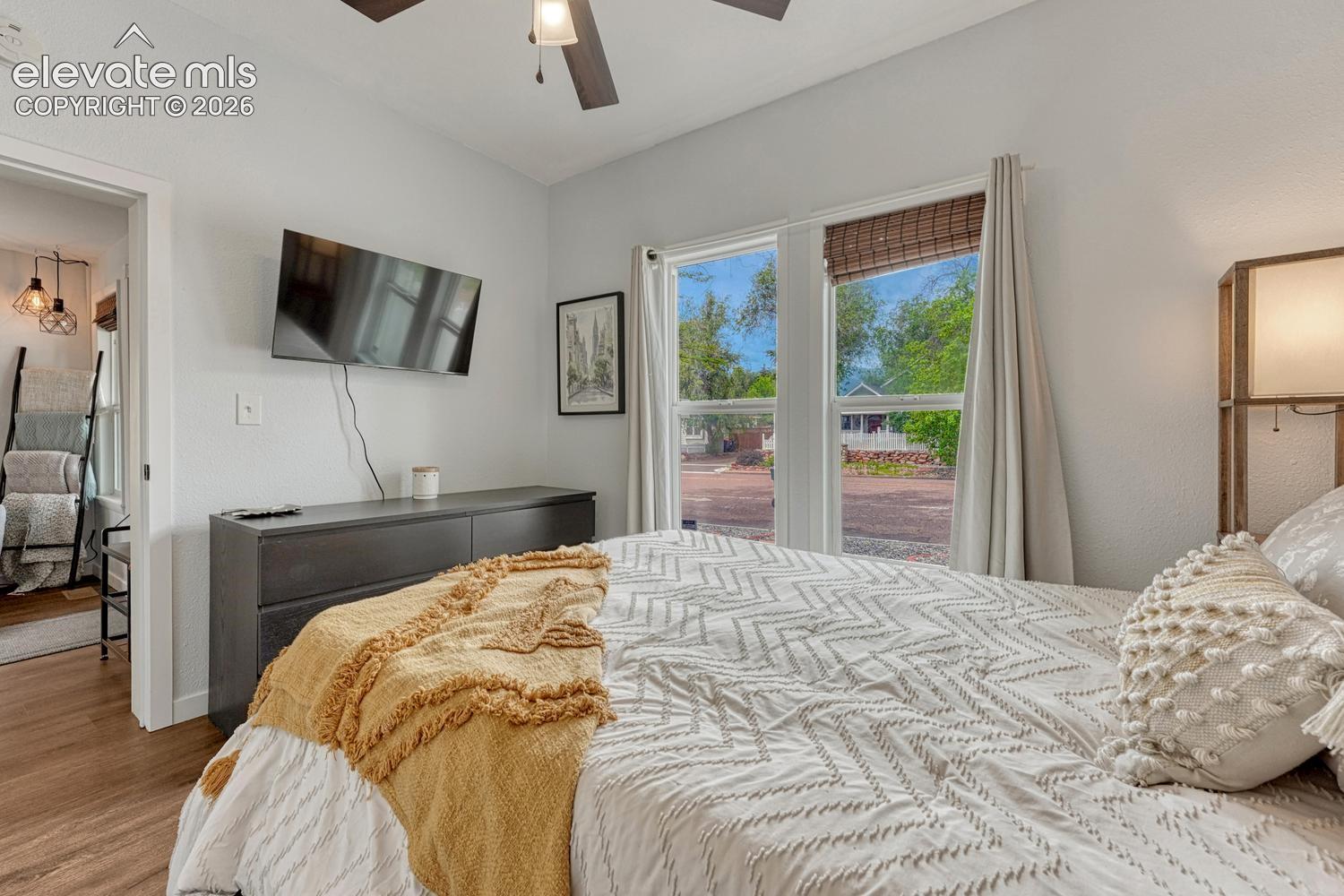 bright and sunny with ceiling fan, wood-finish flooring, white walls, and a window with blinds
