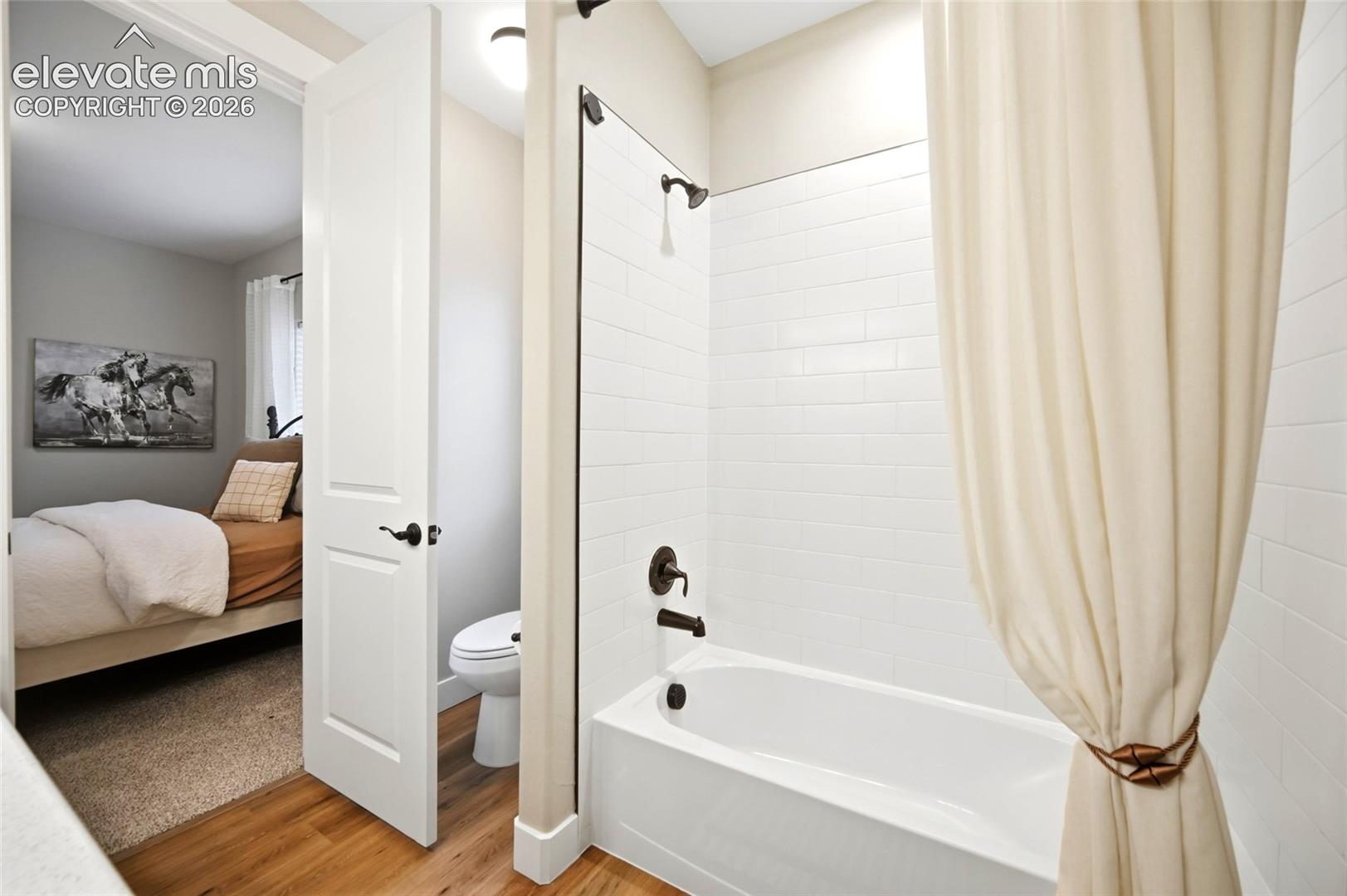 Bathroom featuring white subway tile tub surround, matte black shower fixtures, wood-finish flooring, and a two-panel interior door