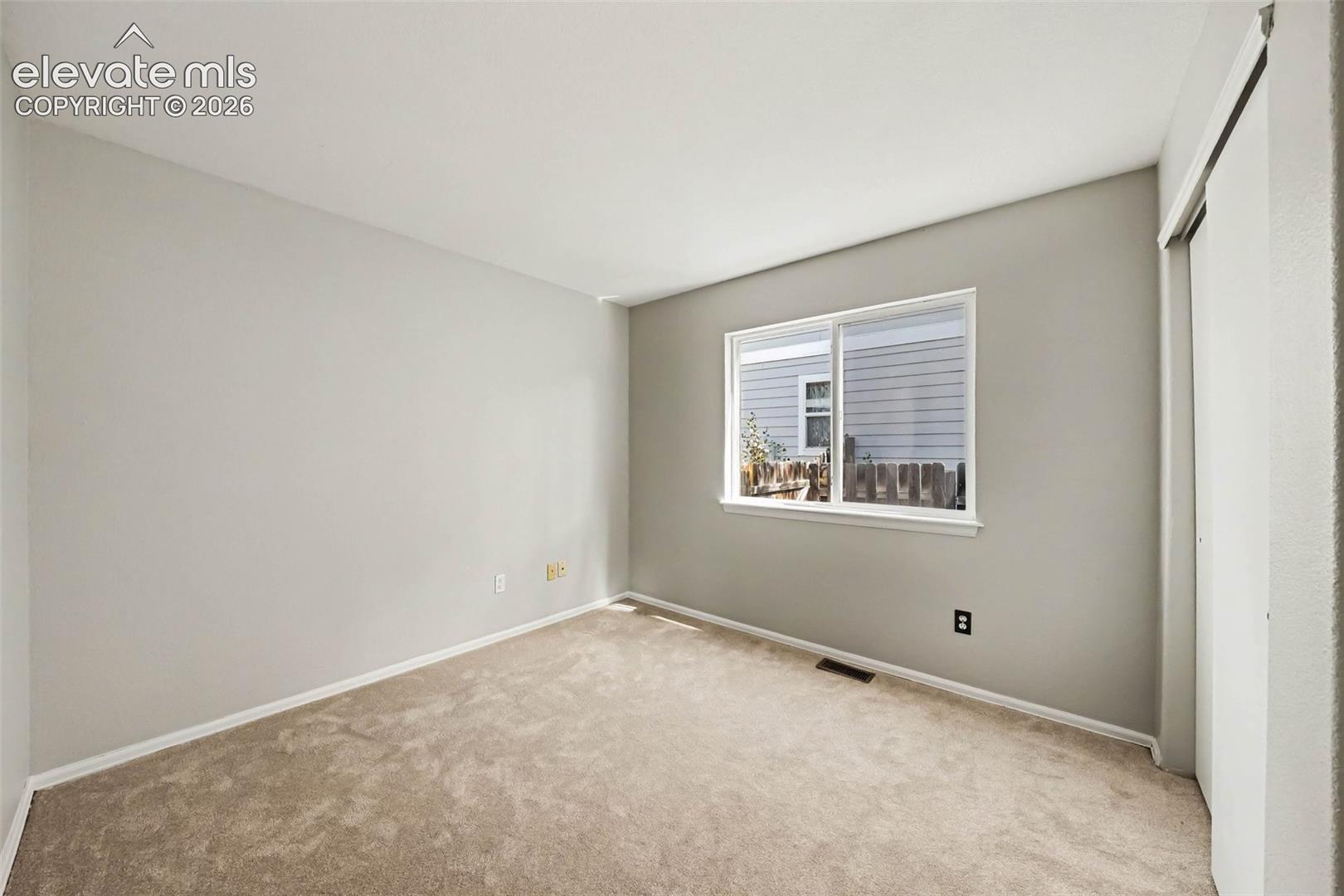 Carpeted flooring, neutral wall color, white trim, sliding closet doors, and a window with white casing