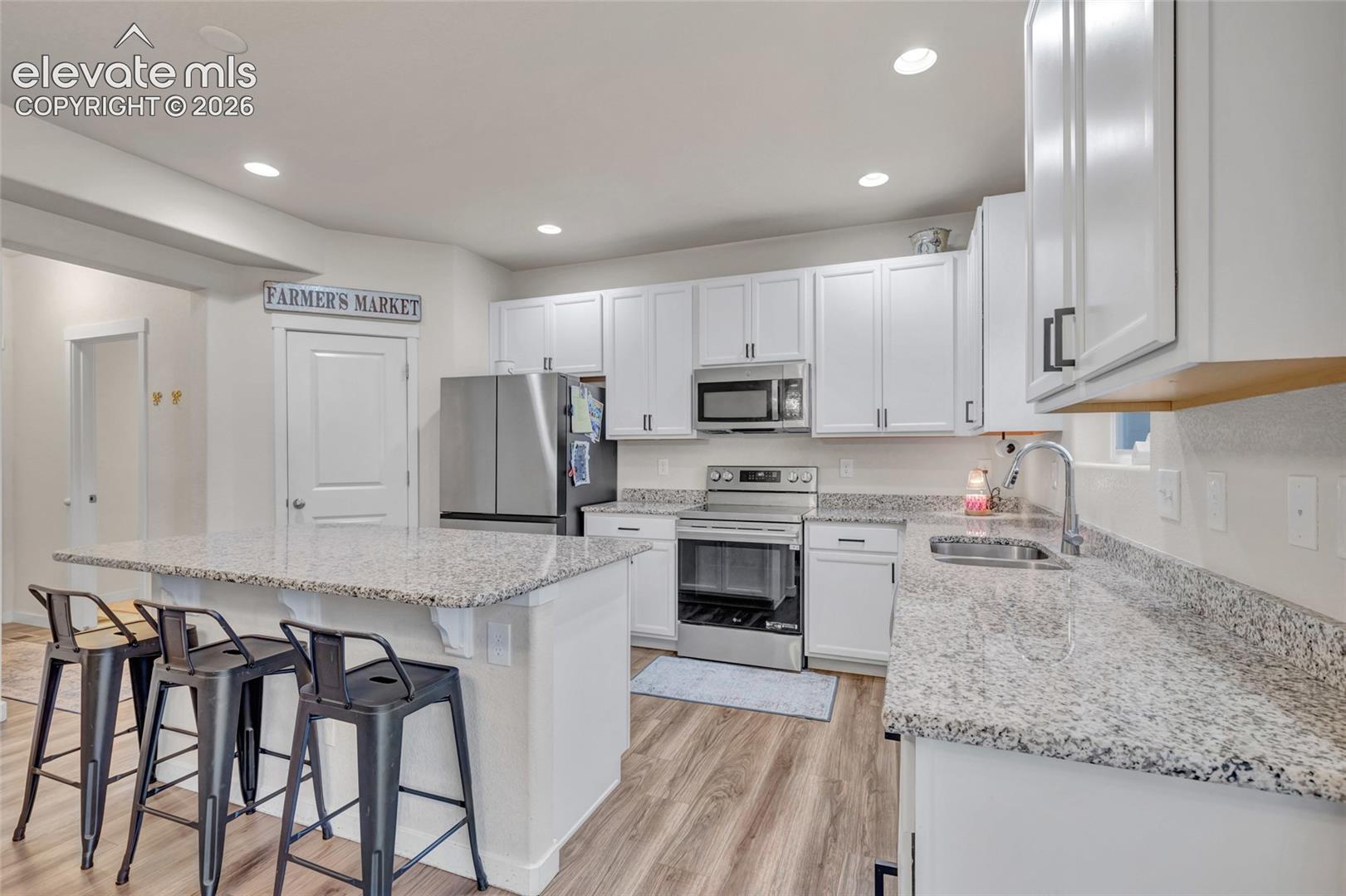 Kitchen featuring light-toned cabinetry, stainless steel appliances, speckled countertops, and wood-finish flooring