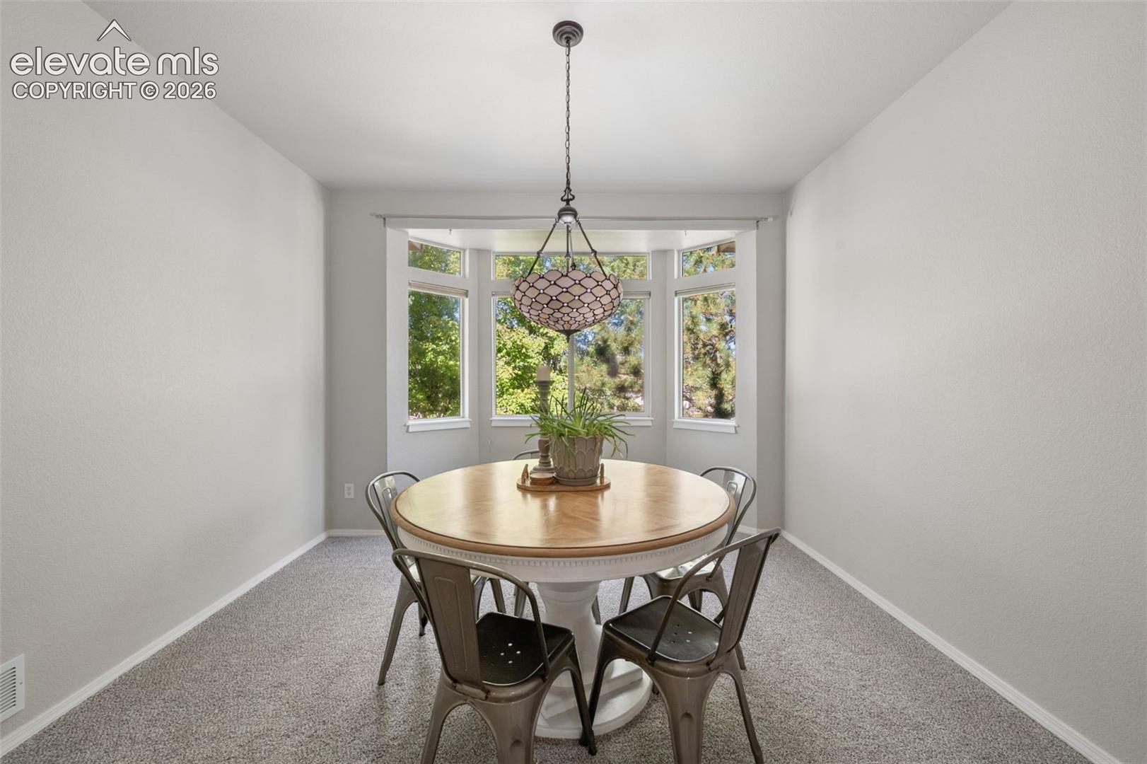 Dining area featuring a bay window, neutral wall paint, carpeted flooring, and a decorative multi-light pendant fixture