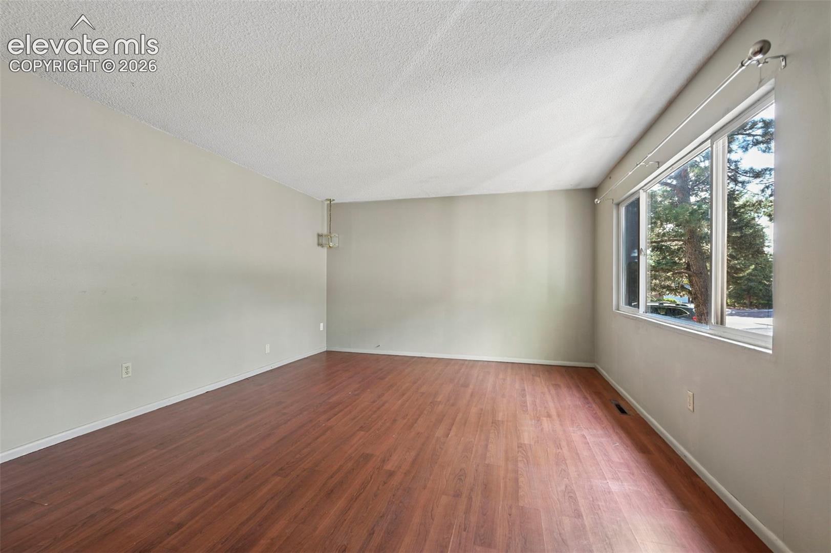 Spacious room featuring wood-finish flooring, light-toned walls, and a textured ceiling