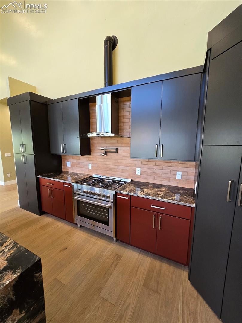 Kitchen with light hardwood / wood-style floors, tasteful backsplash, dark stone counters, and stainless steel range oven