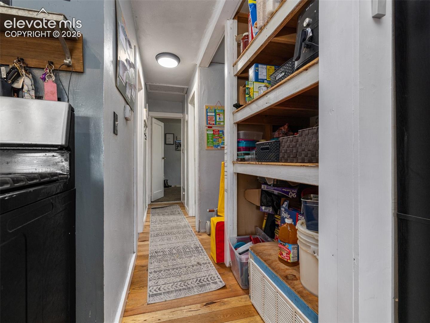 Efficient galley-style hallway with wood-finish flooring, built-in shelving with wood-stained frames displaying organized storage, and recessed ceiling lighting
