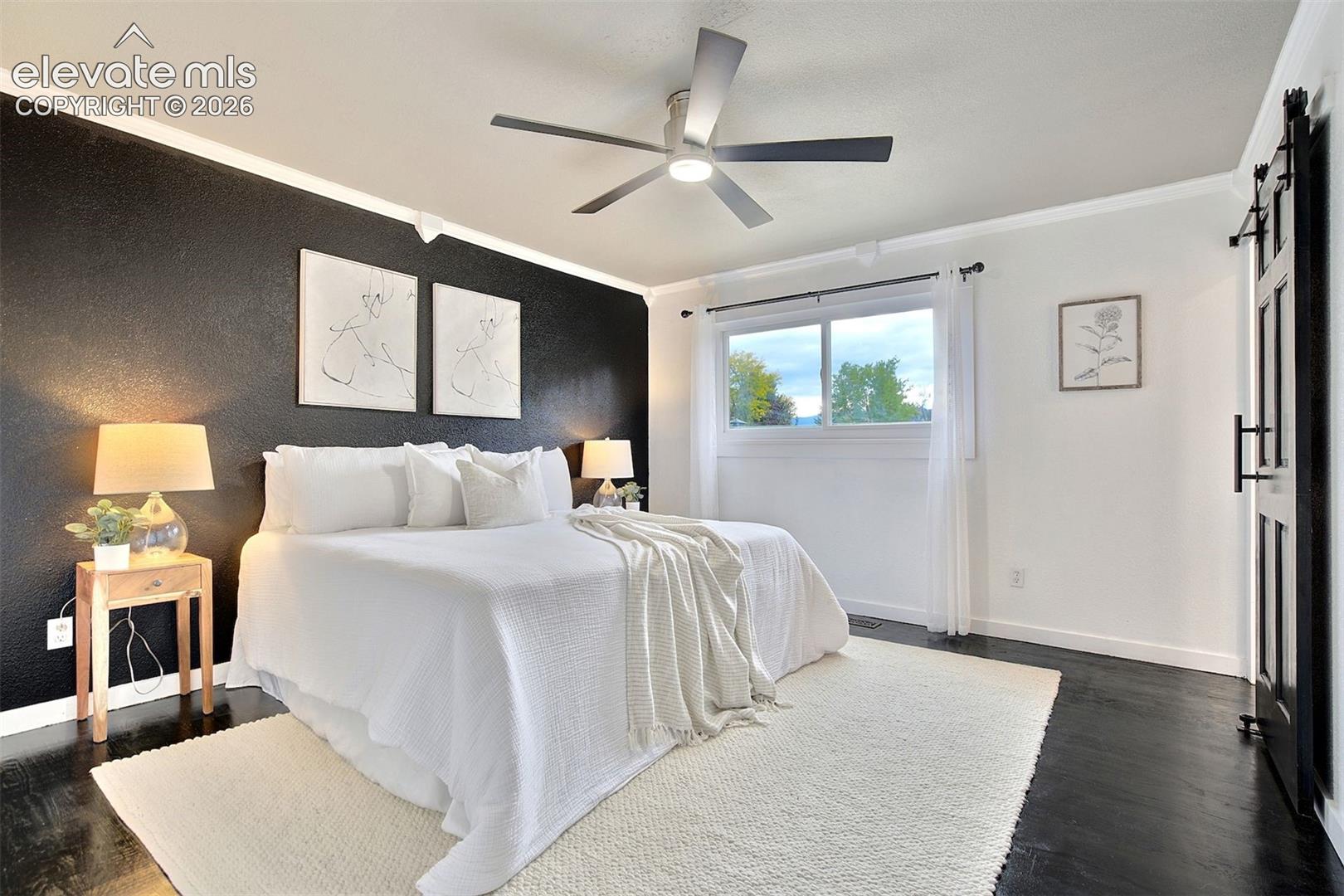Interior space featuring dark-finished wood flooring, a textured black accent wall, a central ceiling fan with integrated lighting, and a black sliding barn-style door