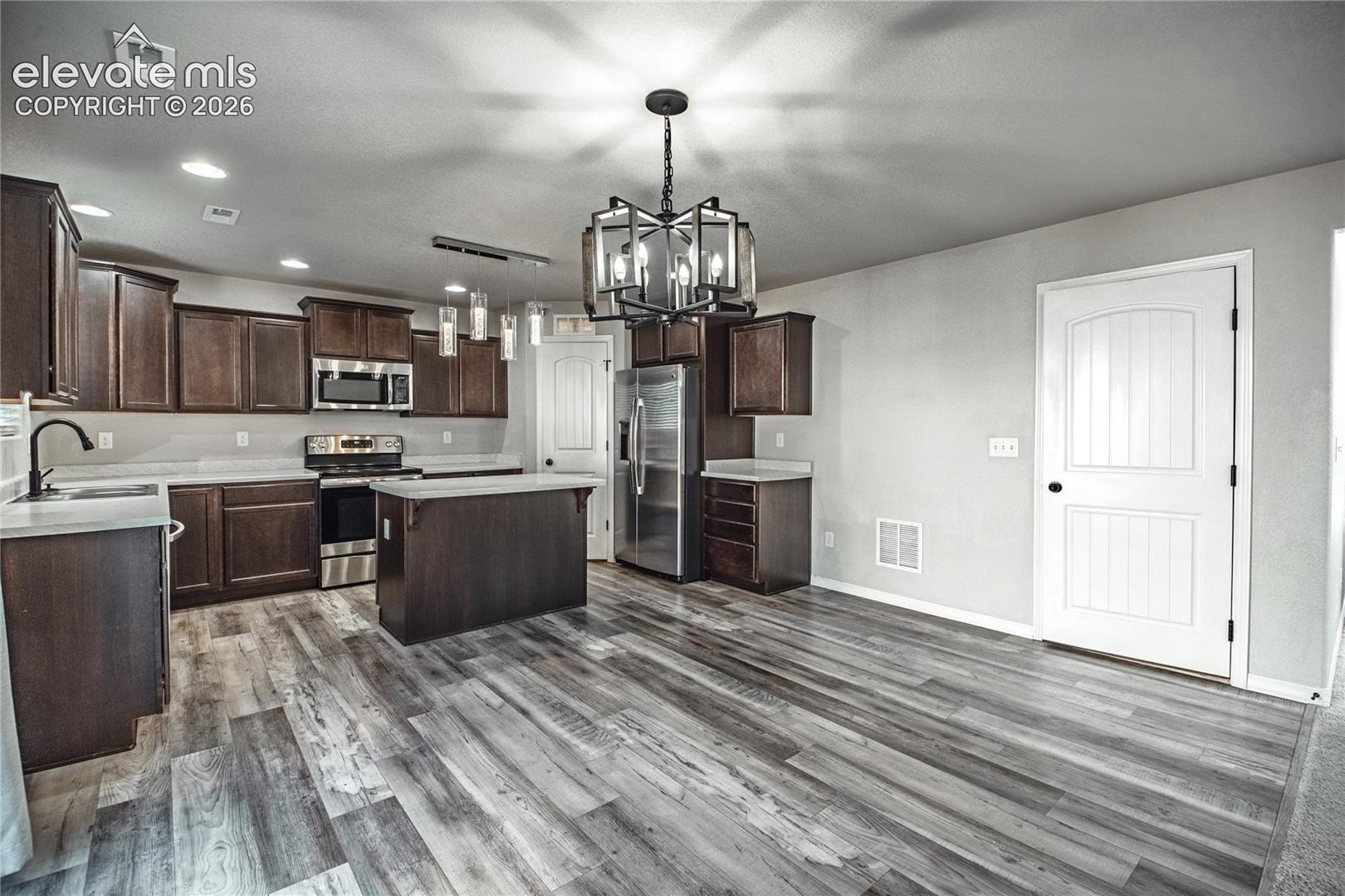 Wood-finish flooring throughout, dark wood-finish cabinetry, stainless steel appliances, a center island, and recessed lighting