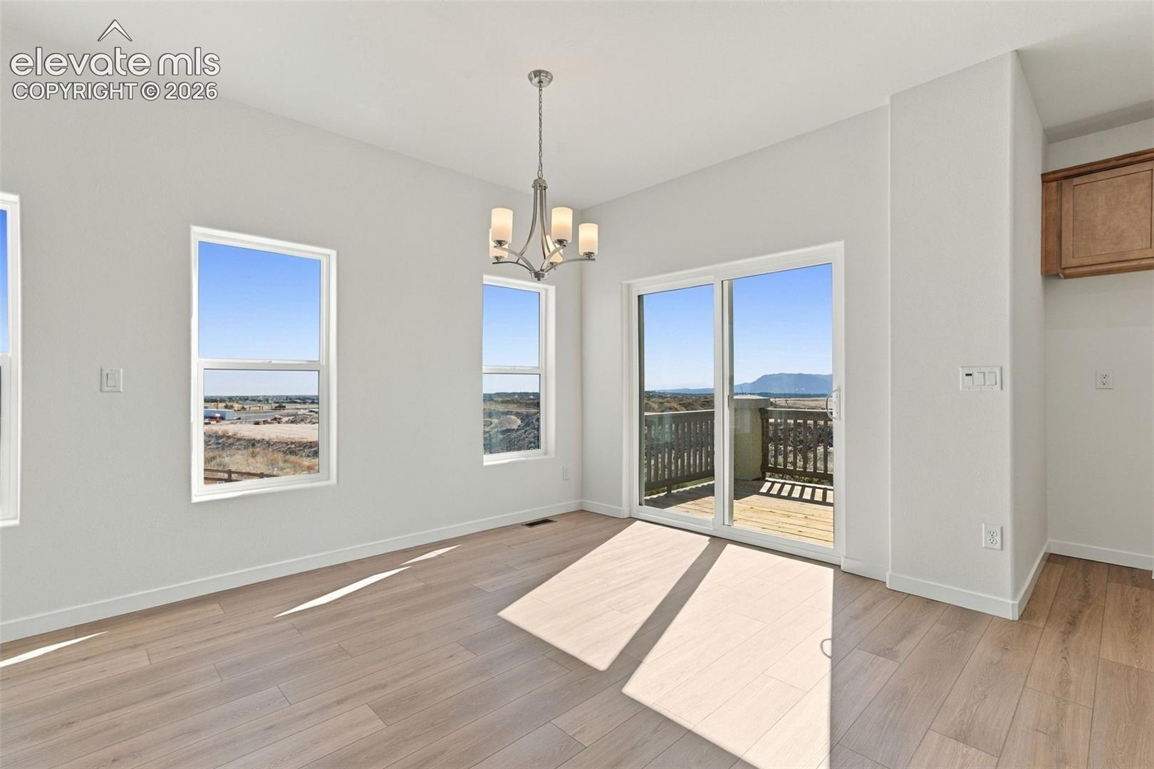 Light wood-finish flooring with a flush-mount chandelier, multiple large windows, and a sliding glass door opening to an outdoor deck