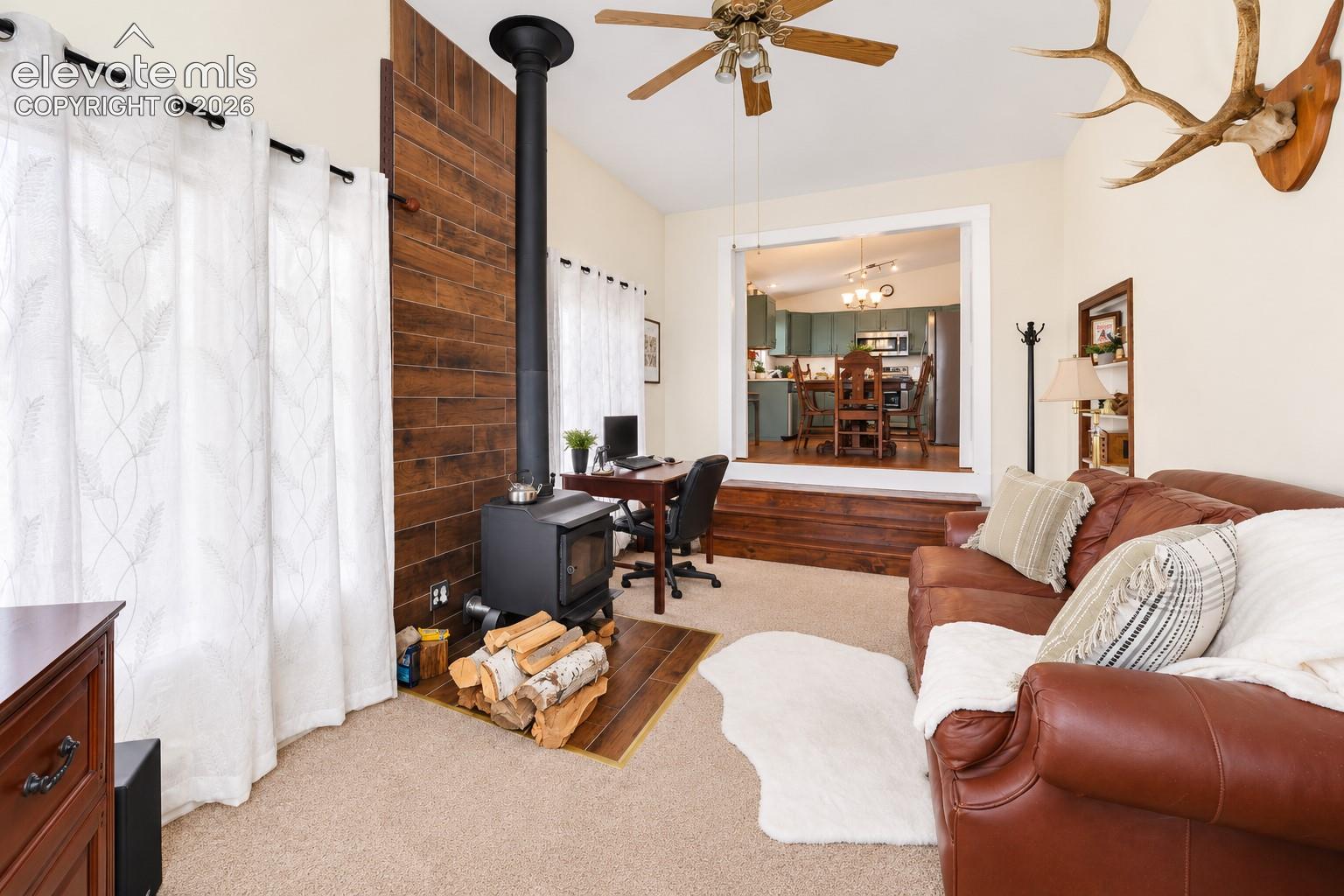 Wood-burning stove with vertical hearth piping, wood-plank accent wall, ceiling fan, and built-in wall shelving