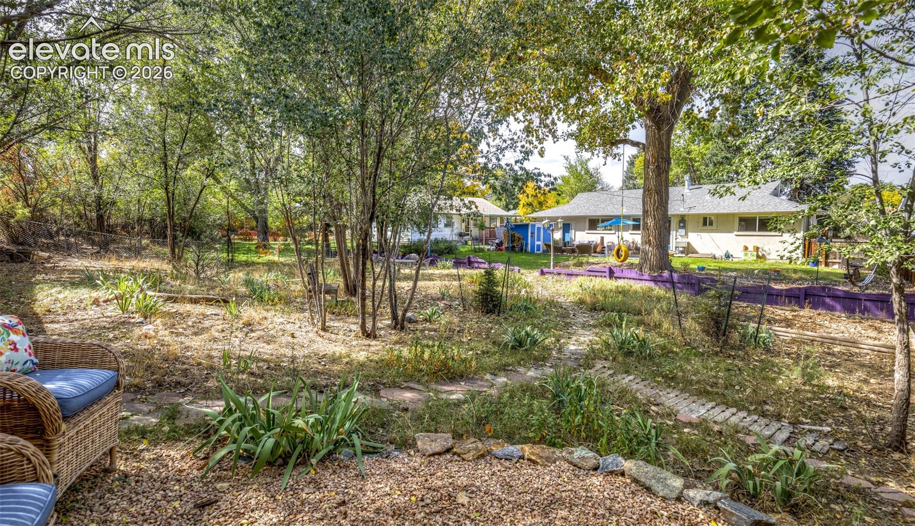 Expansive backyard featuring mature trees, a gravel patio, and stone-edged garden beds