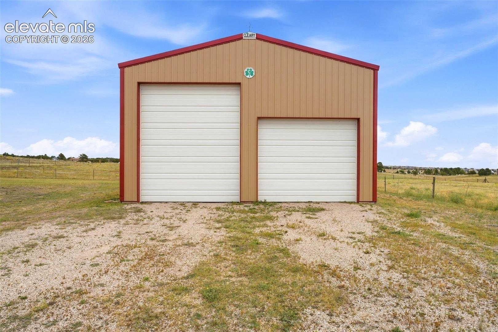 Metal-sided outbuilding with a two-bay design, featuring a larger and smaller garage door