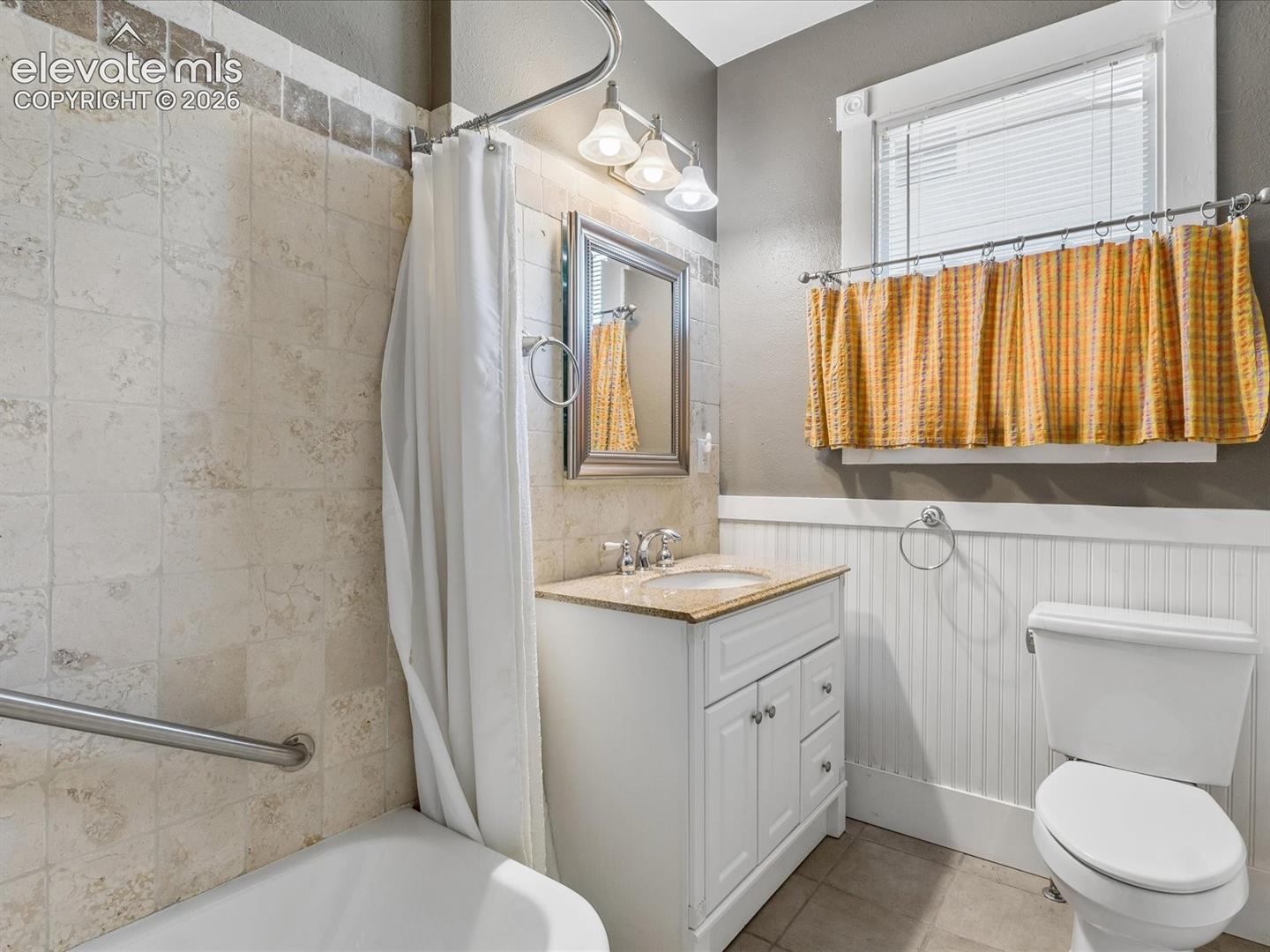 Bathroom featuring a white vanity with a light-toned countertop, a shower/tub combination with tiled surround, and white beadboard paneling
