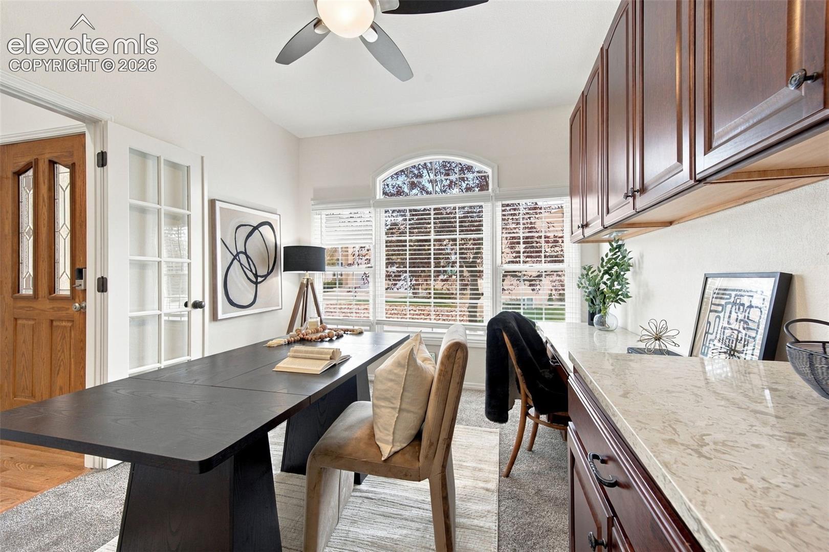 Custom built-in cabinetry featuring dark wood finishes, stone-composite countertops, arched window detailing, integrated ceiling fan, and solid wood-frame entry door with glass paneling