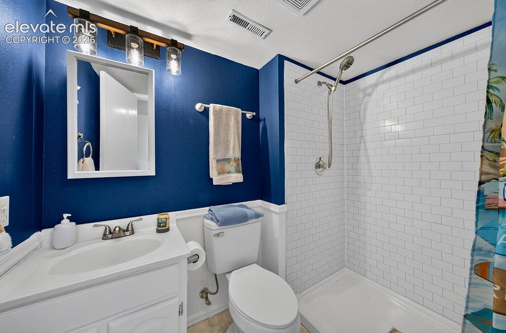 White vanity with integrated sink, subway tile shower surround, chrome shower fixtures, and overhead lighting