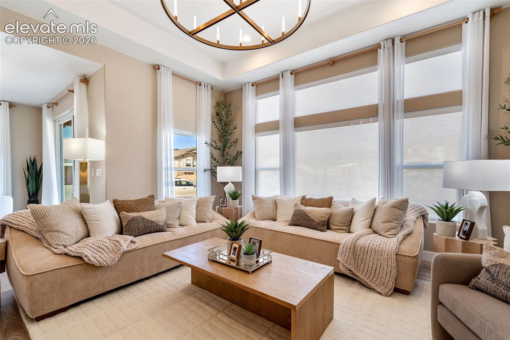 Living area featuring a tray ceiling, expansive windows with transoms, and a large circular metal chandelier
