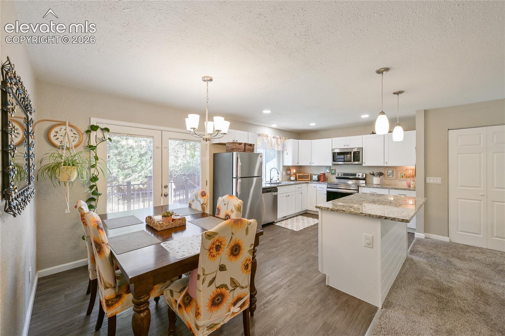 Kitchen featuring white shaker-style cabinetry, stone-surface countertops, a center island with pendant lighting, and wood-finish flooring