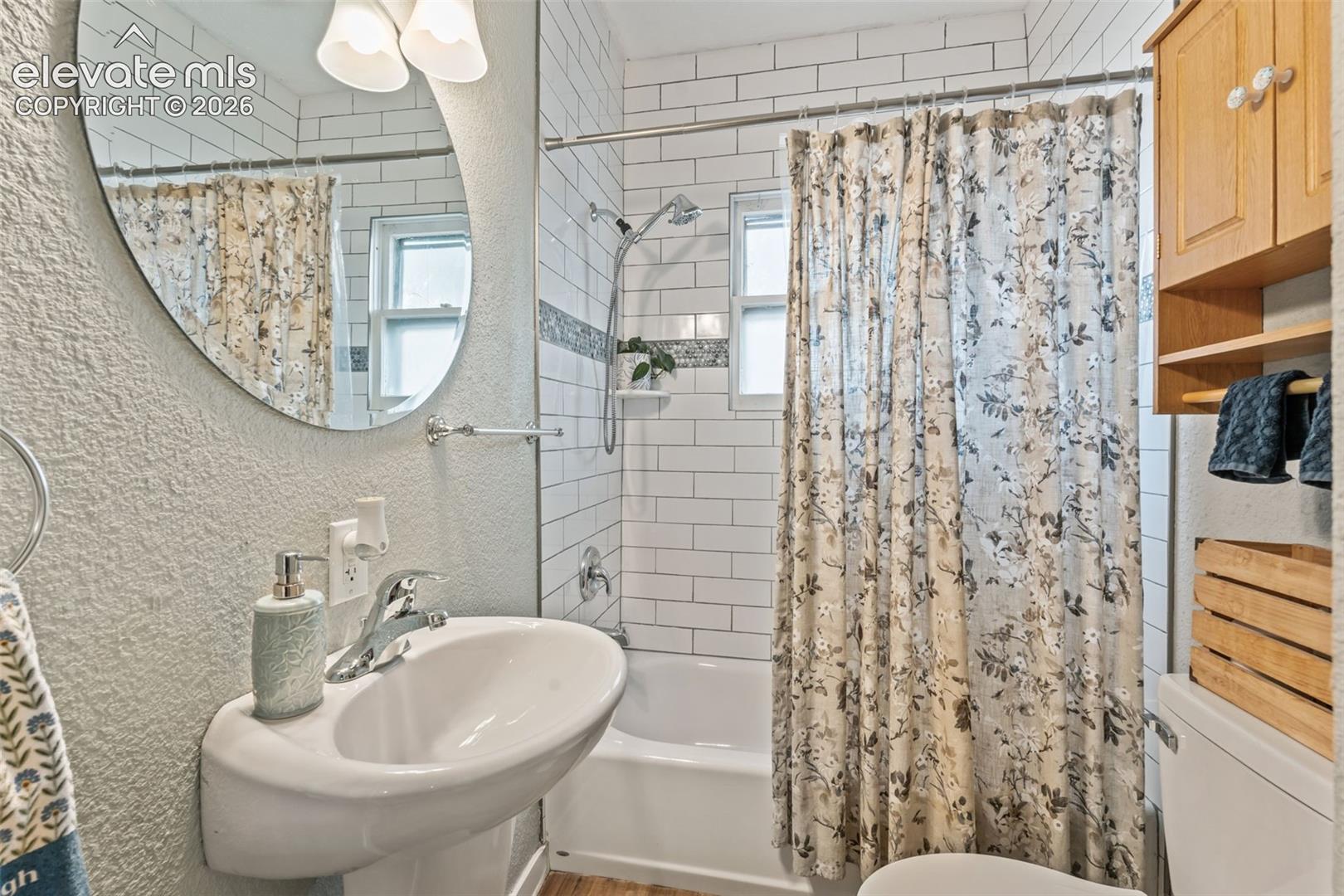 Bathroom featuring a white subway tile shower surround with an accent tile band, a pedestal sink, and a wall-mounted oval mirror