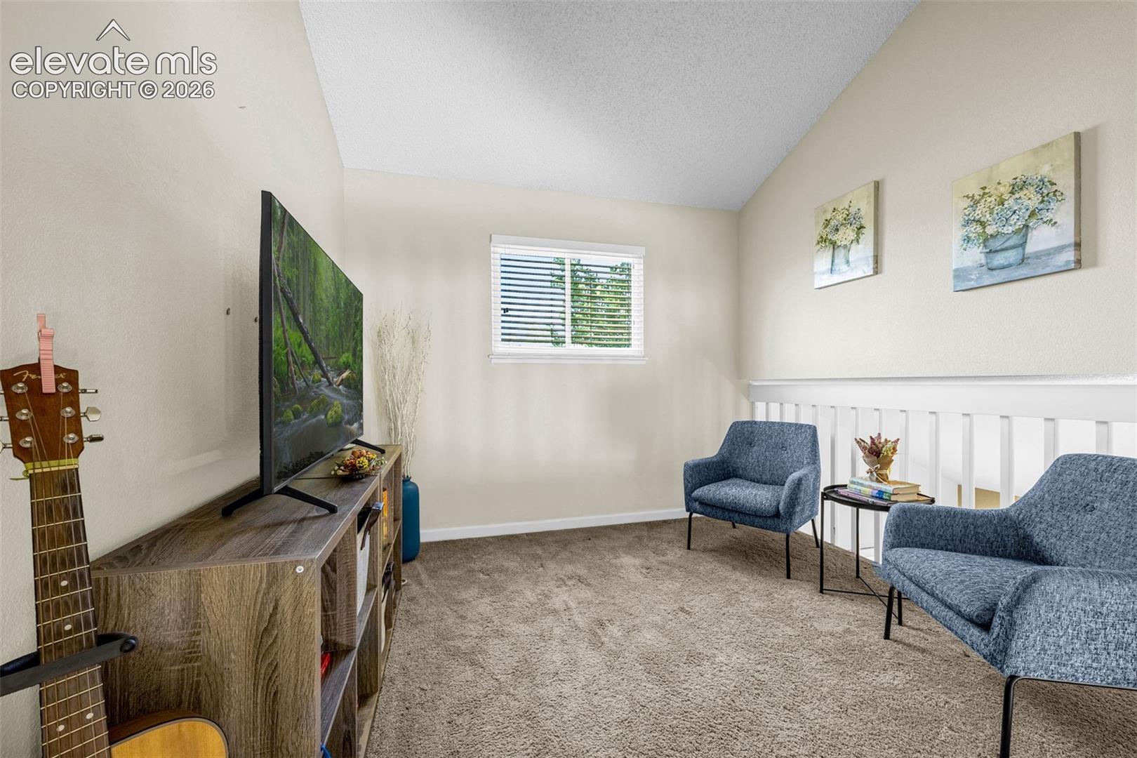 Room featuring a vaulted ceiling, neutral wall coloring, carpeted flooring, a horizontal sliding window, and a white wooden balustrade