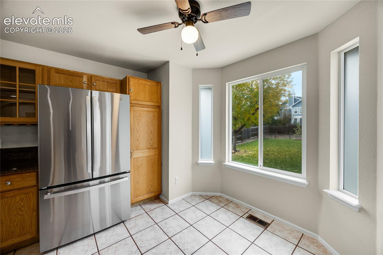 Kitchen space featuring wood cabinetry, stainless steel French-door refrigerator, tile flooring, and a bay window configuration