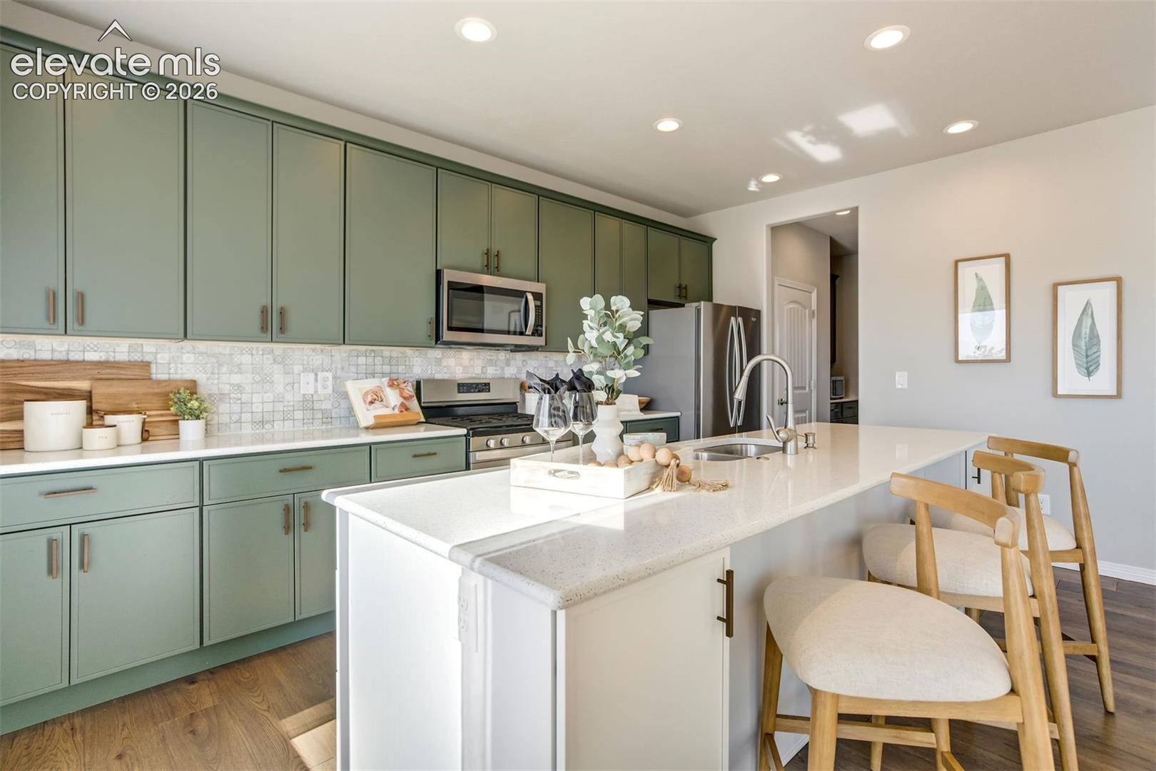 Kitchen featuring green cabinetry, stainless steel appliances, a white tile backsplash, a large island with a sink, and recessed lighting