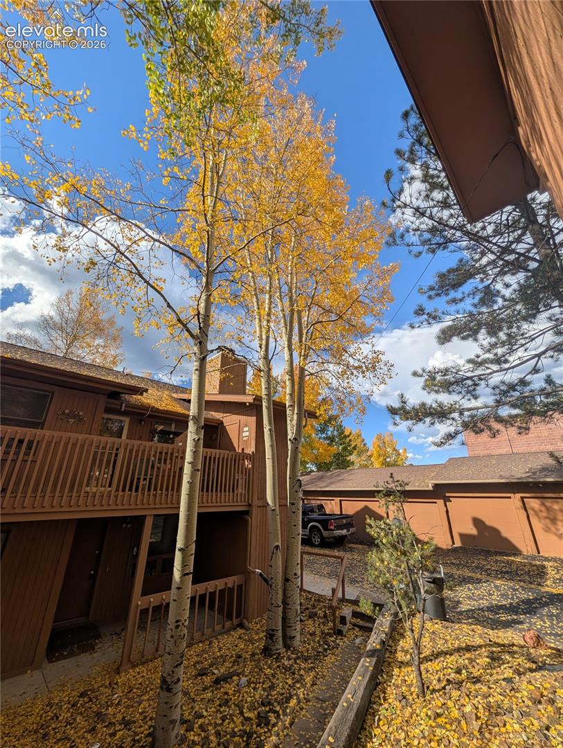 Rustic mountain retreat featuring mature aspen trees with golden fall foliage, multi-level wood-sided construction with wraparound decking, and expansive grounds with natural landscaping and outbuildings