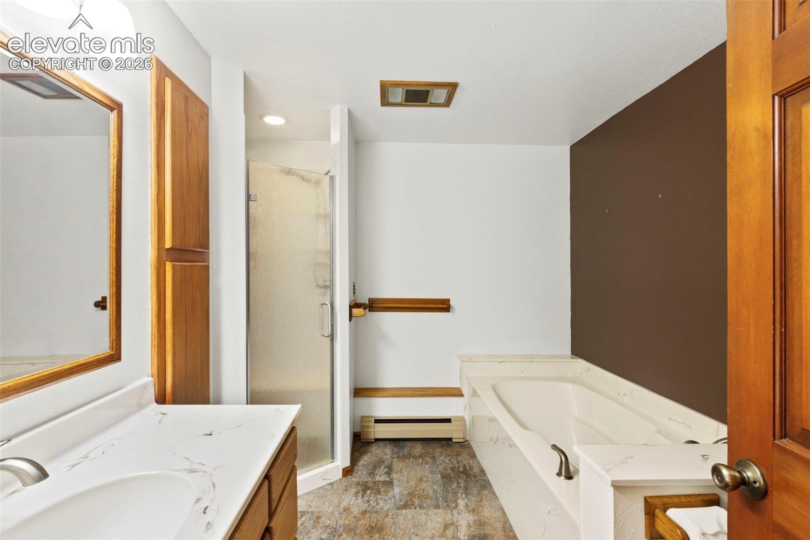 Bathroom featuring a vanity with a white stone-patterned countertop, a separate stall shower with a glass door, a built-in soaking tub with stone-patterned surround, and wood-finish cabinetry