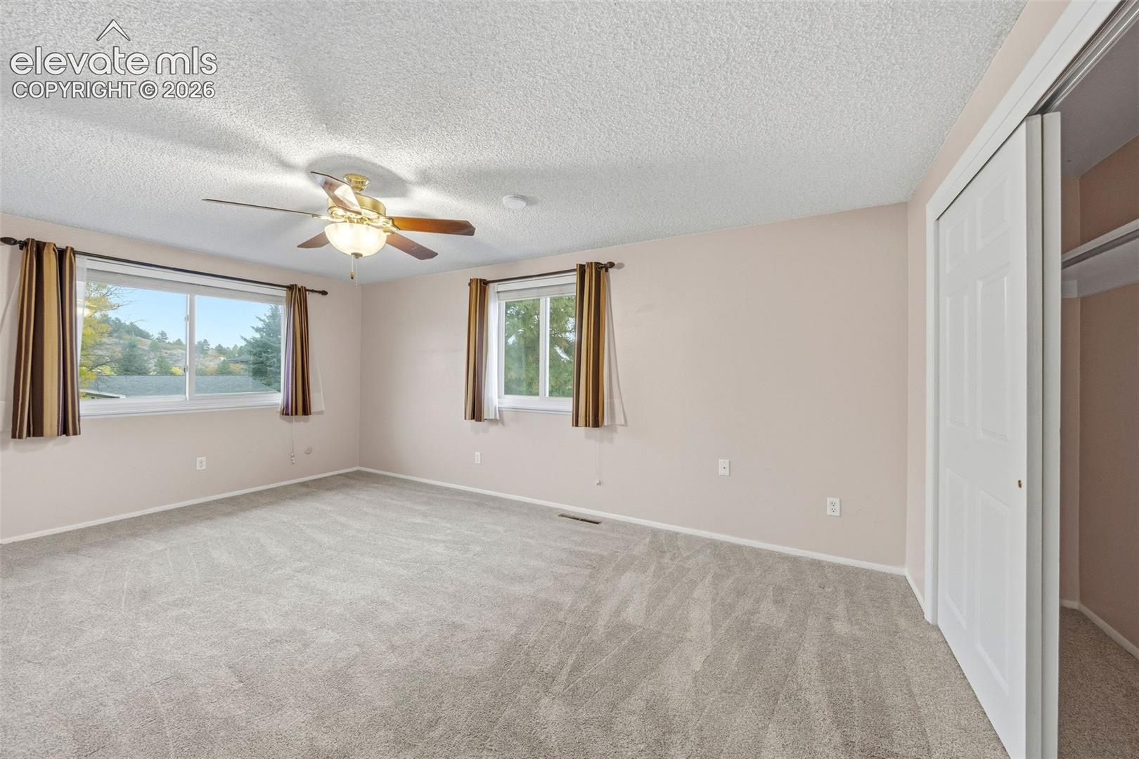 Bedroom featuring neutral-toned carpeting, dual windows, a ceiling fan with integrated lighting, and a closet with a bifold door