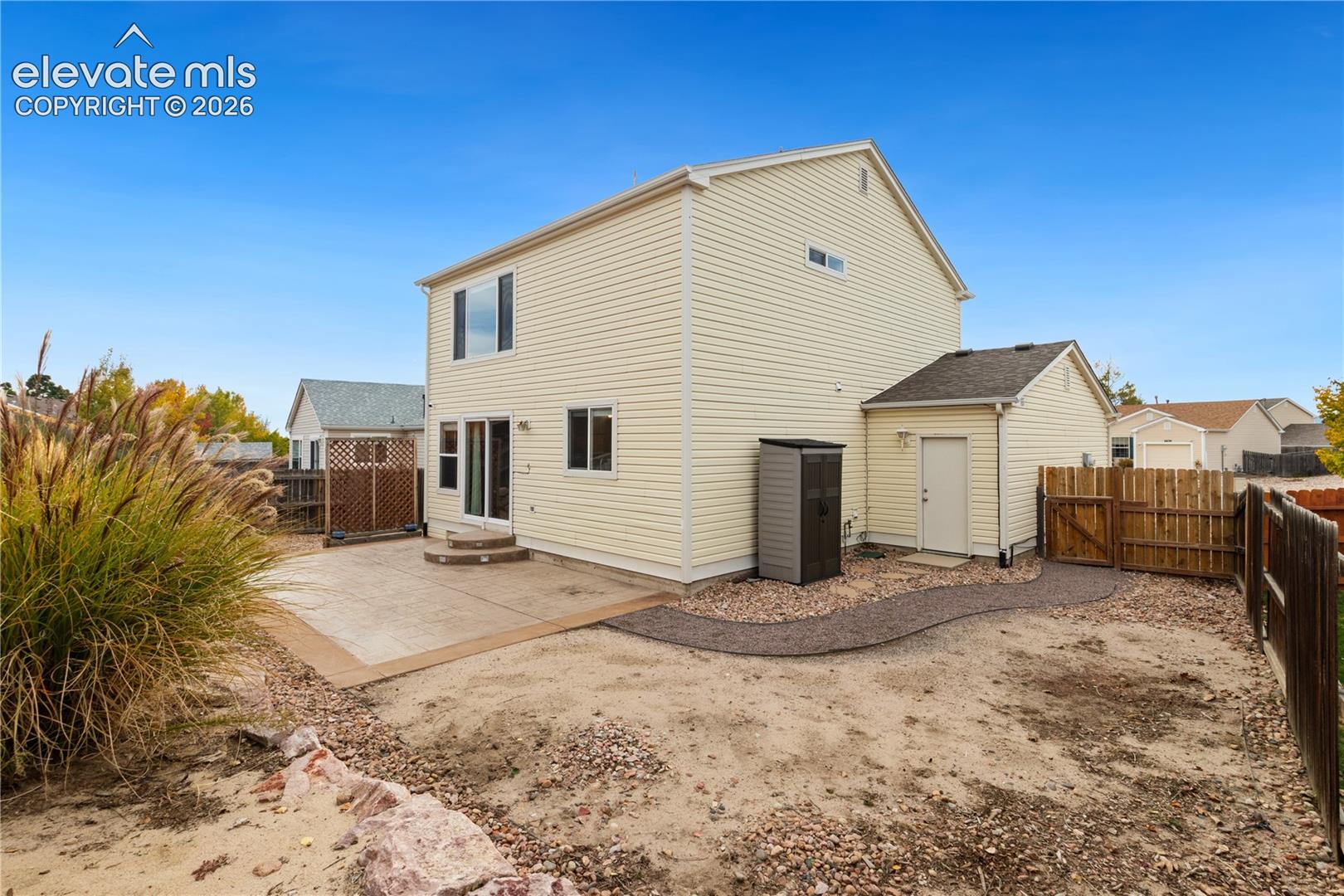 Two-story exterior featuring light-colored horizontal siding, a rear concrete patio, a dedicated storage entrance, and wood privacy fencing