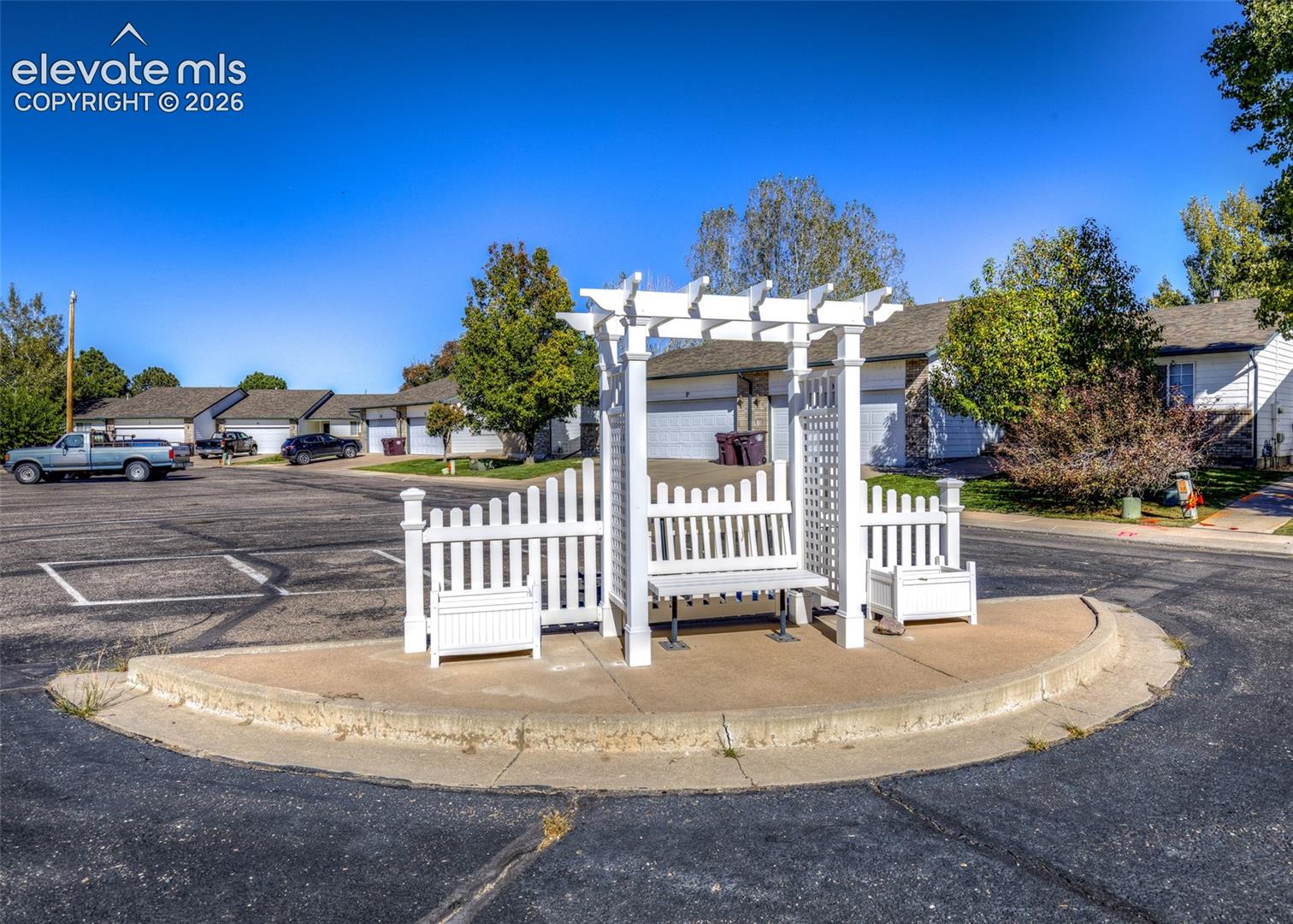White vinyl pergola featuring integrated trellis panels, a built-in bench, and side planter boxes situated on a concrete pedestal