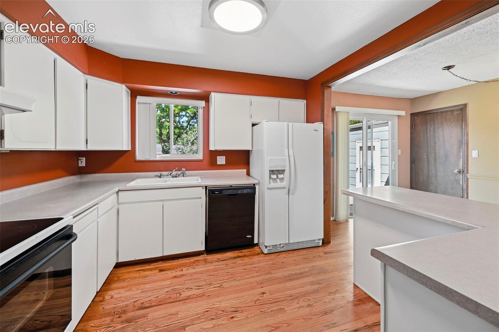 Kitchen featuring white cabinetry, wood-finish flooring, a white composite sink, and a built-in dishwasher