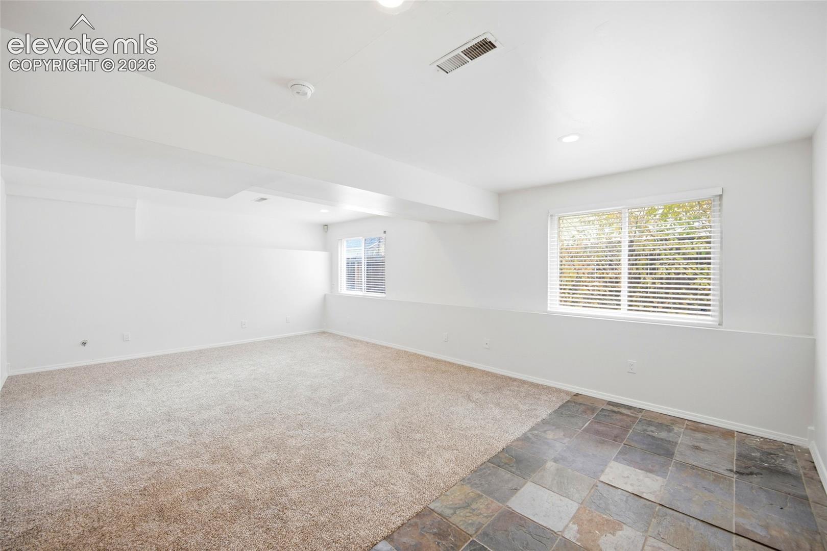 Interior space featuring neutral wall-to-wall carpeting, multi-toned stone tile flooring, recessed lighting, and dual windows with horizontal blinds