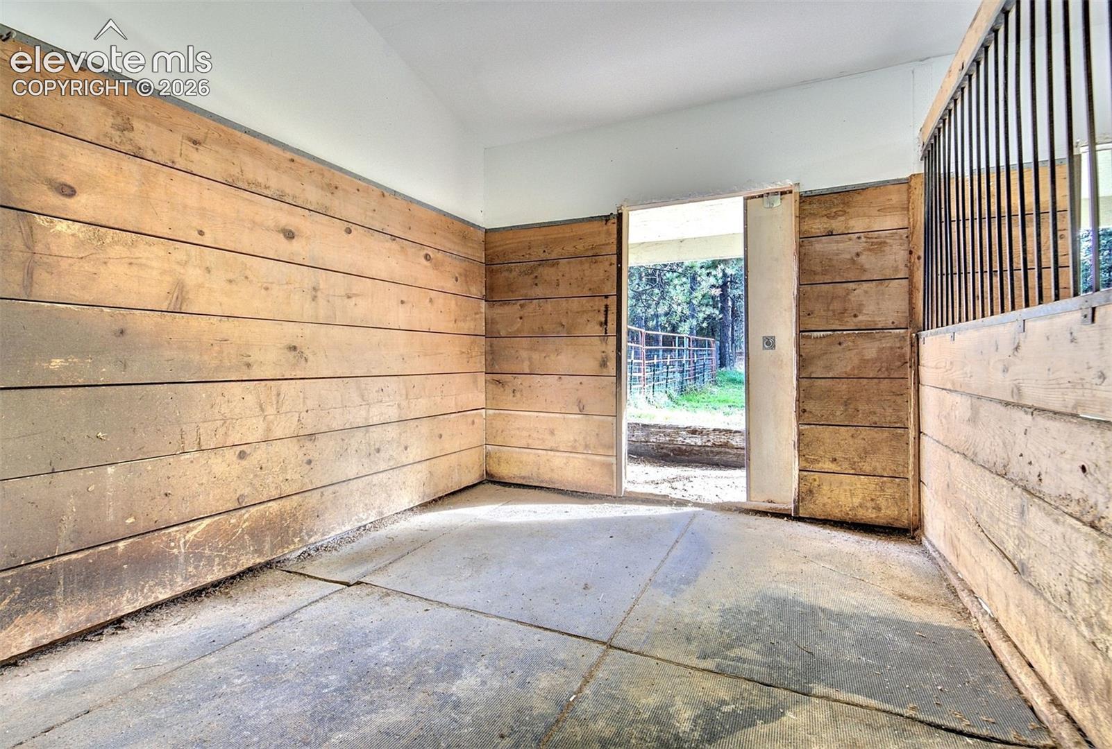 Stall featuring horizontal wood-plank walls, concrete flooring, and metal bar partitioning