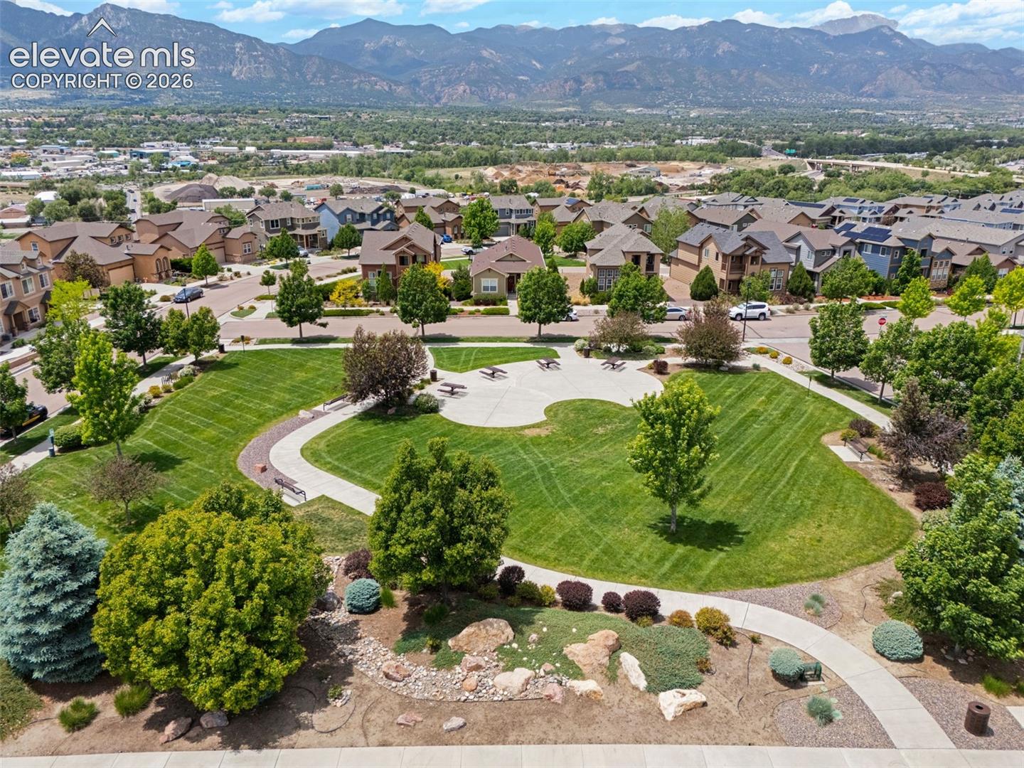 Expansive community park 1/2 block from the subject property with green space featuring manicured lawns, mature trees, concrete pathways, and dedicated seating areas with mountain scenery