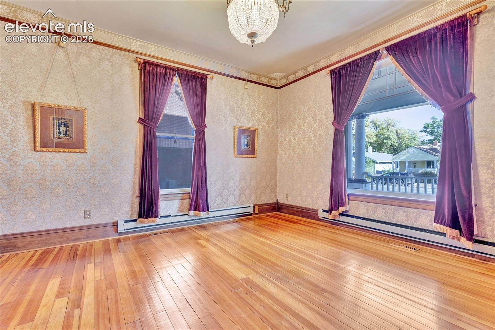 Polished wood-finish flooring, intricate patterned wallpaper, crown molding, dark wood trim, and a decorative crystal chandelier