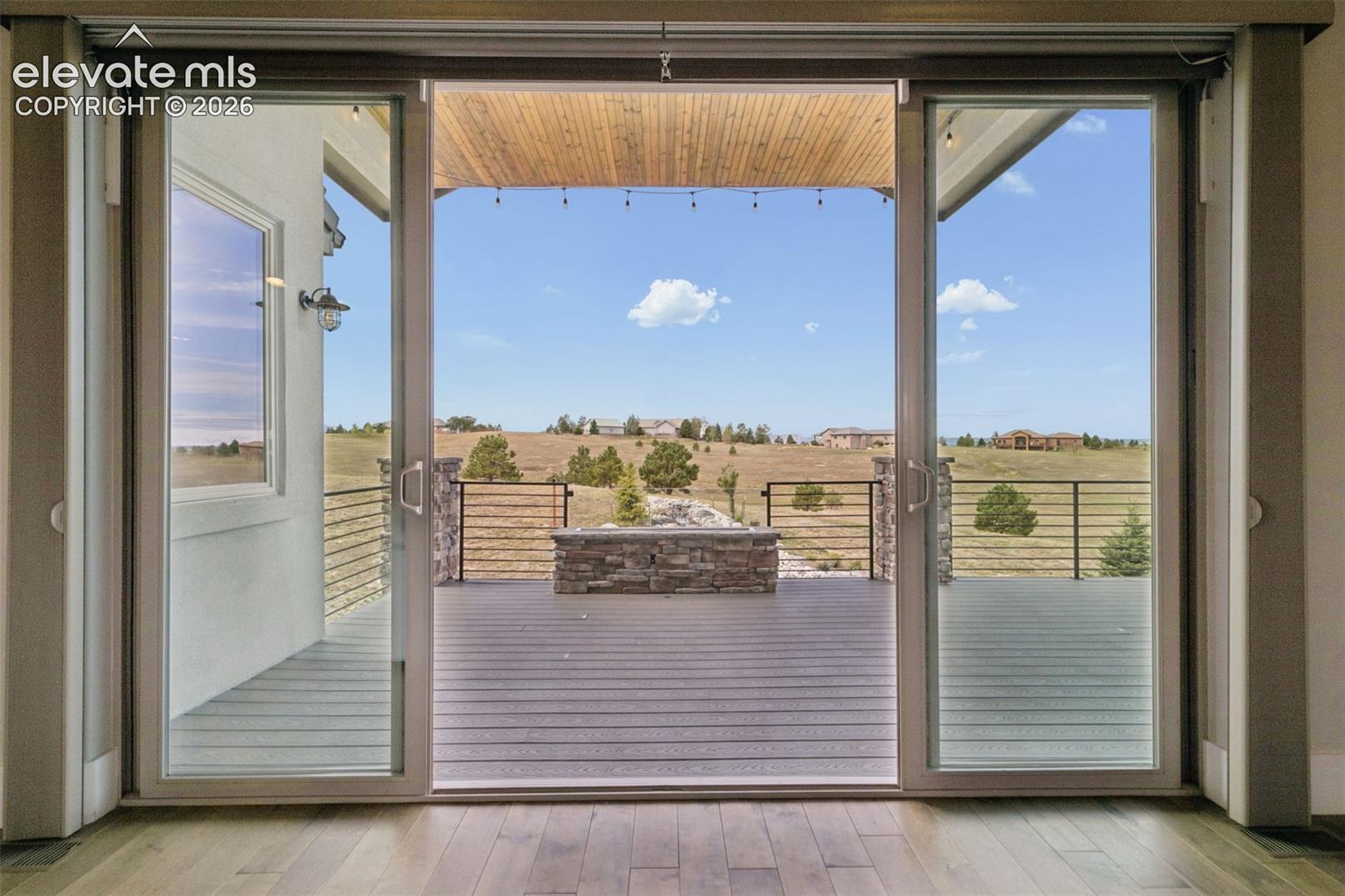 Sliding glass doors opening to an outdoor deck with a stone-clad fire pit, wood-finish flooring, and a natural landscape