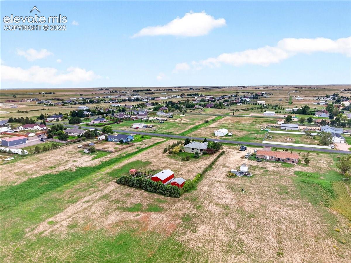 Aerial perspective of expansive acreage featuring open pasture land, established perimeter vegetation, and red outbuildings