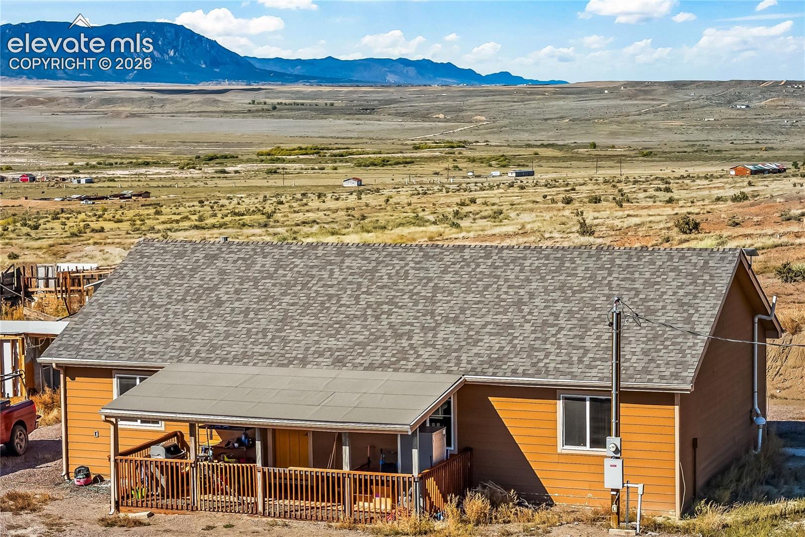 Exterior featuring horizontal siding, a pitched asphalt shingle roof, and a covered front porch with wooden railing, set against a backdrop of mountainous terrain