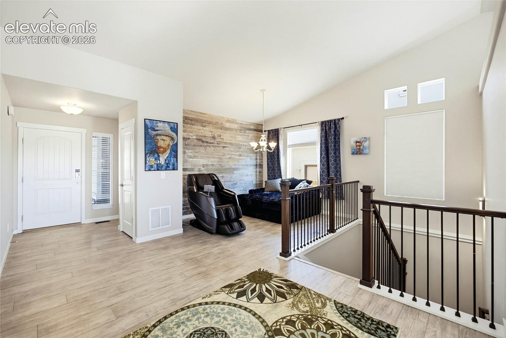 Vaulted ceilings, wood-finish flooring, a wood-panel accent wall, and a staircase with dark wood handrails and vertical balusters