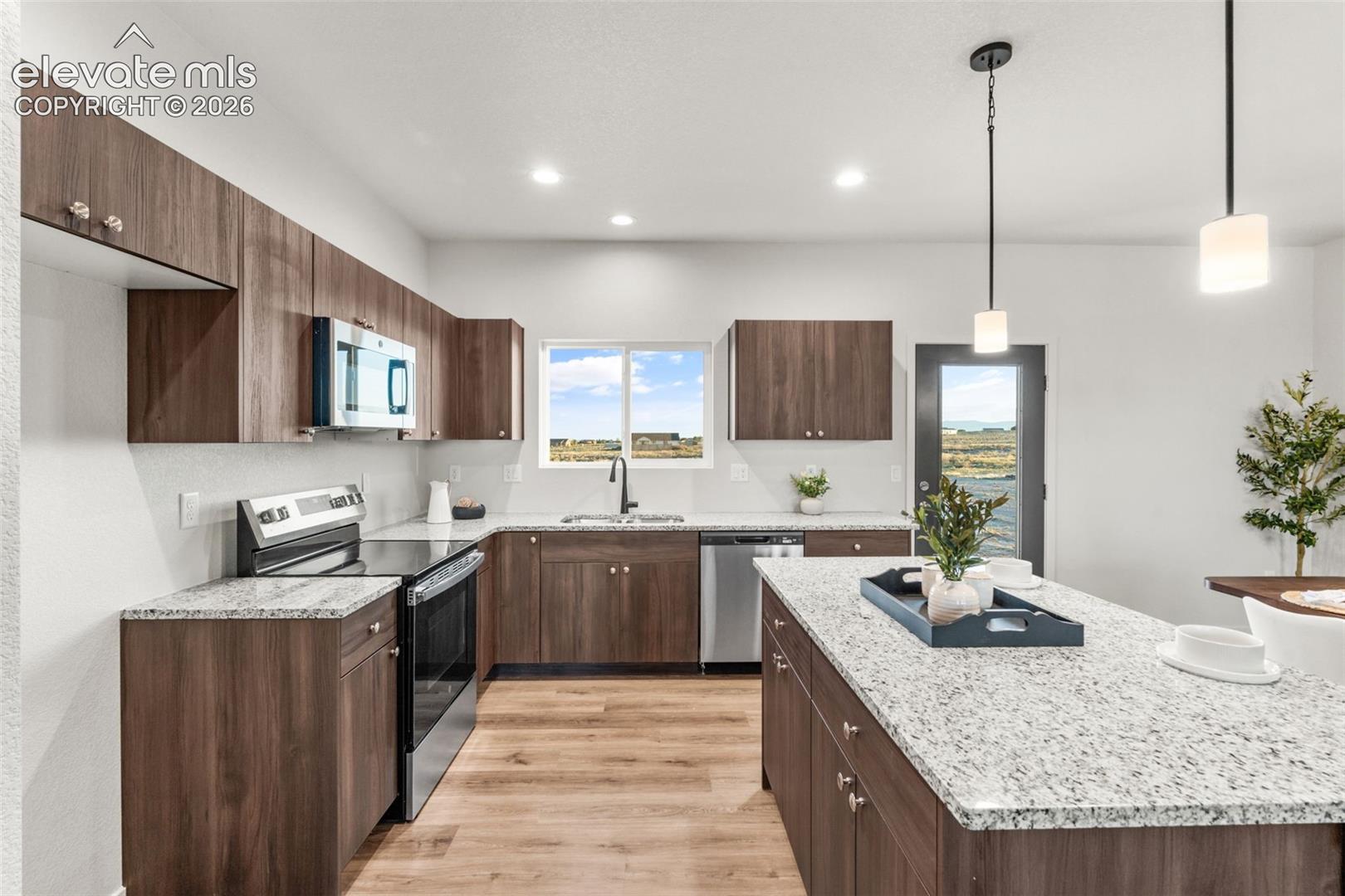 Kitchen featuring wood-finish cabinetry, stone countertops, a center island with pendant lighting, stainless steel appliances, and wood-finish flooring