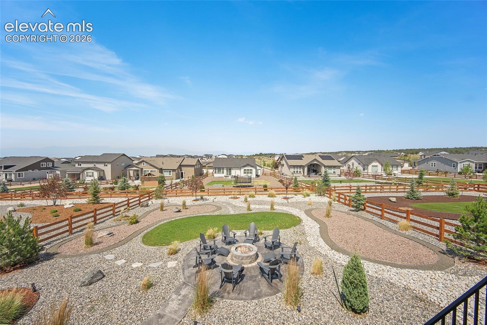 Expansive backyard featuring a stone fire pit, gravel and grass landscaping, decorative wood fencing, and mature plantings