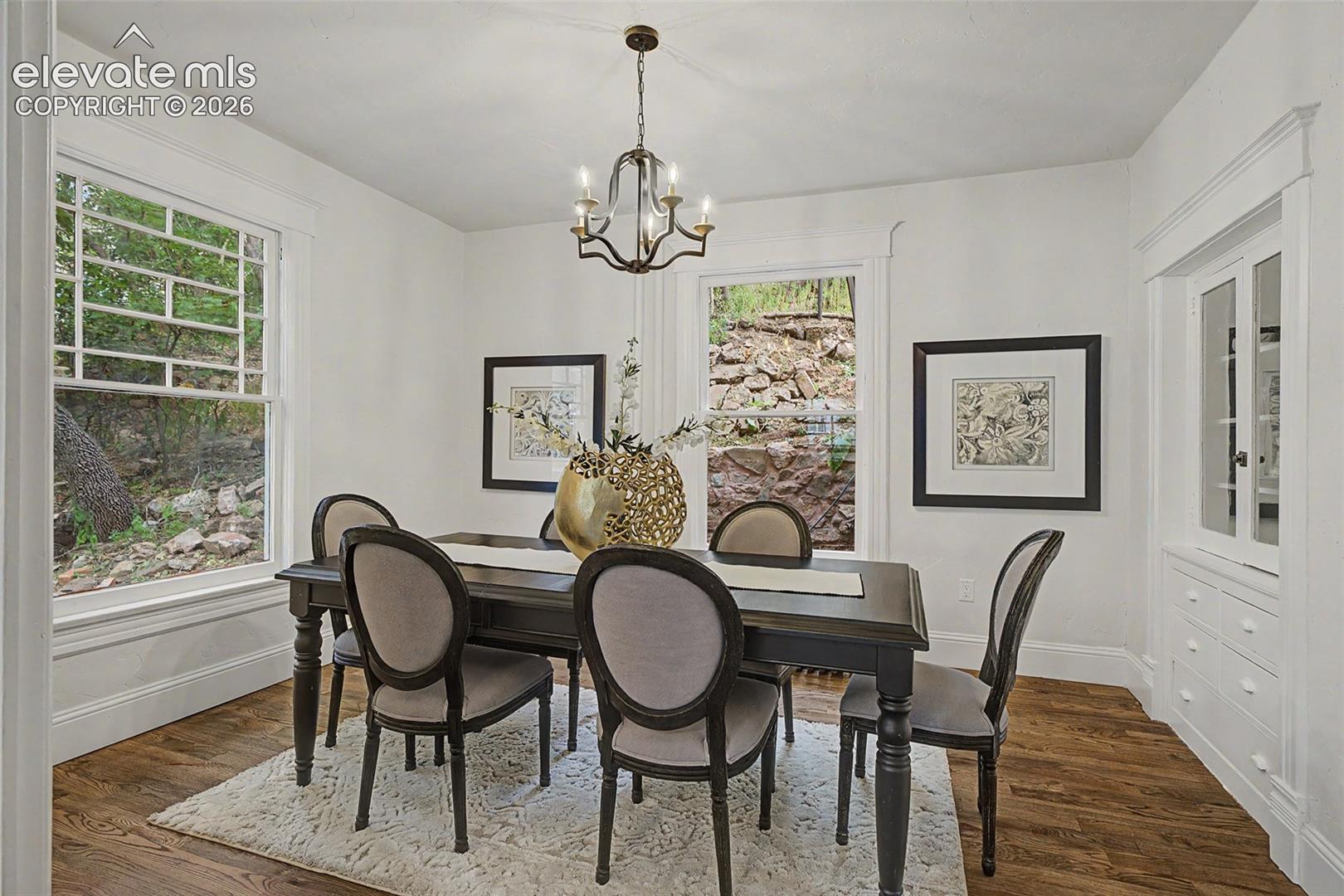 Dining area featuring wood-finish flooring, white walls, and a built-in china cabinet with glass-front doors