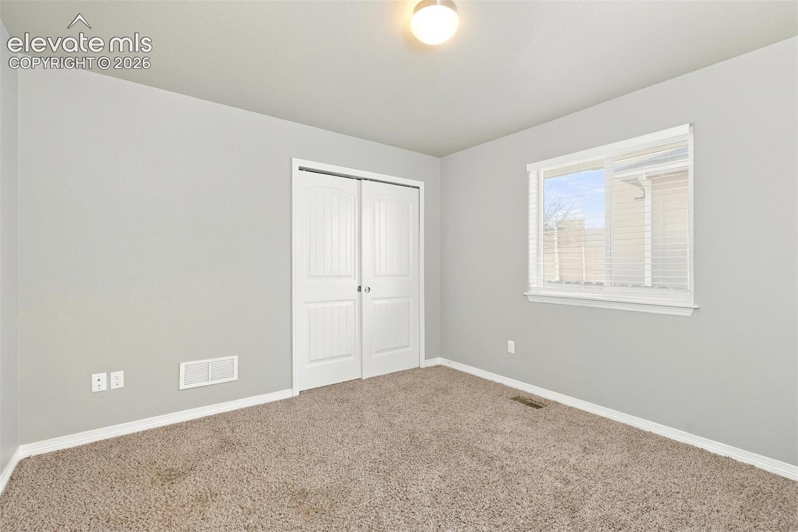 Neutral-toned interior space featuring wall-to-wall carpeting, a dual-panel closet door, and a single-pane sliding window