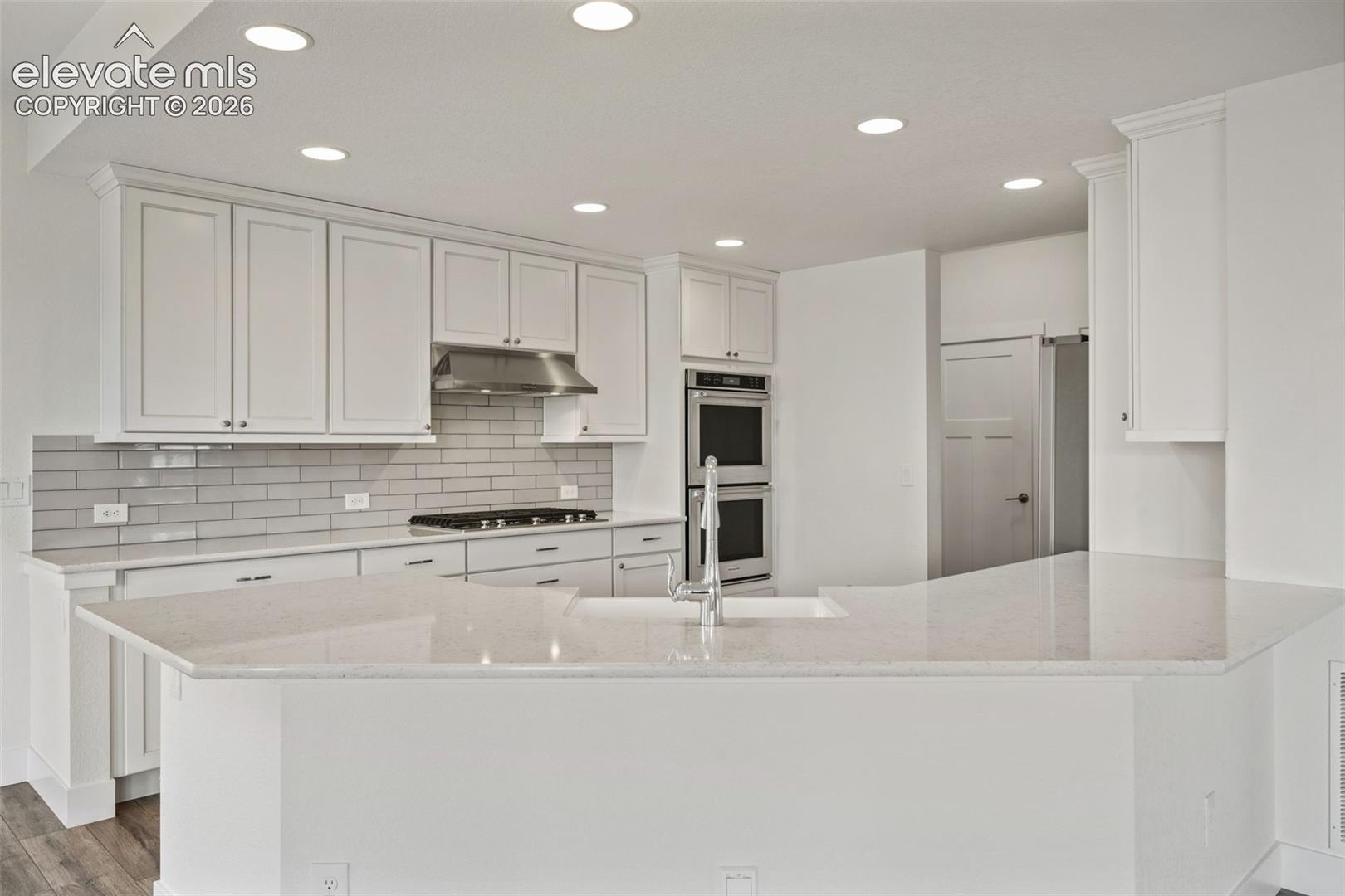 White shaker cabinetry, light-toned countertops, subway tile backsplash, stainless steel gas range, and double wall ovens