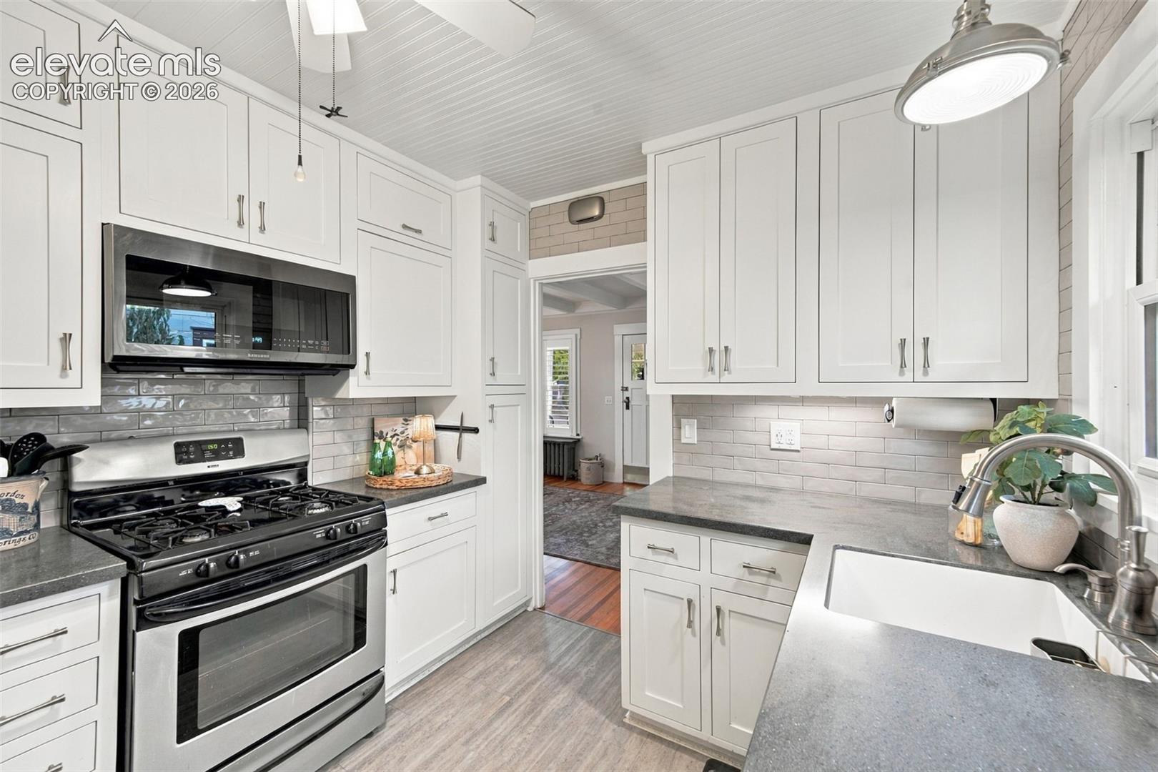 Kitchen featuring white shaker-style cabinetry, stainless steel gas range, stone-finish countertops, apron-front sink, and subway tile backsplash