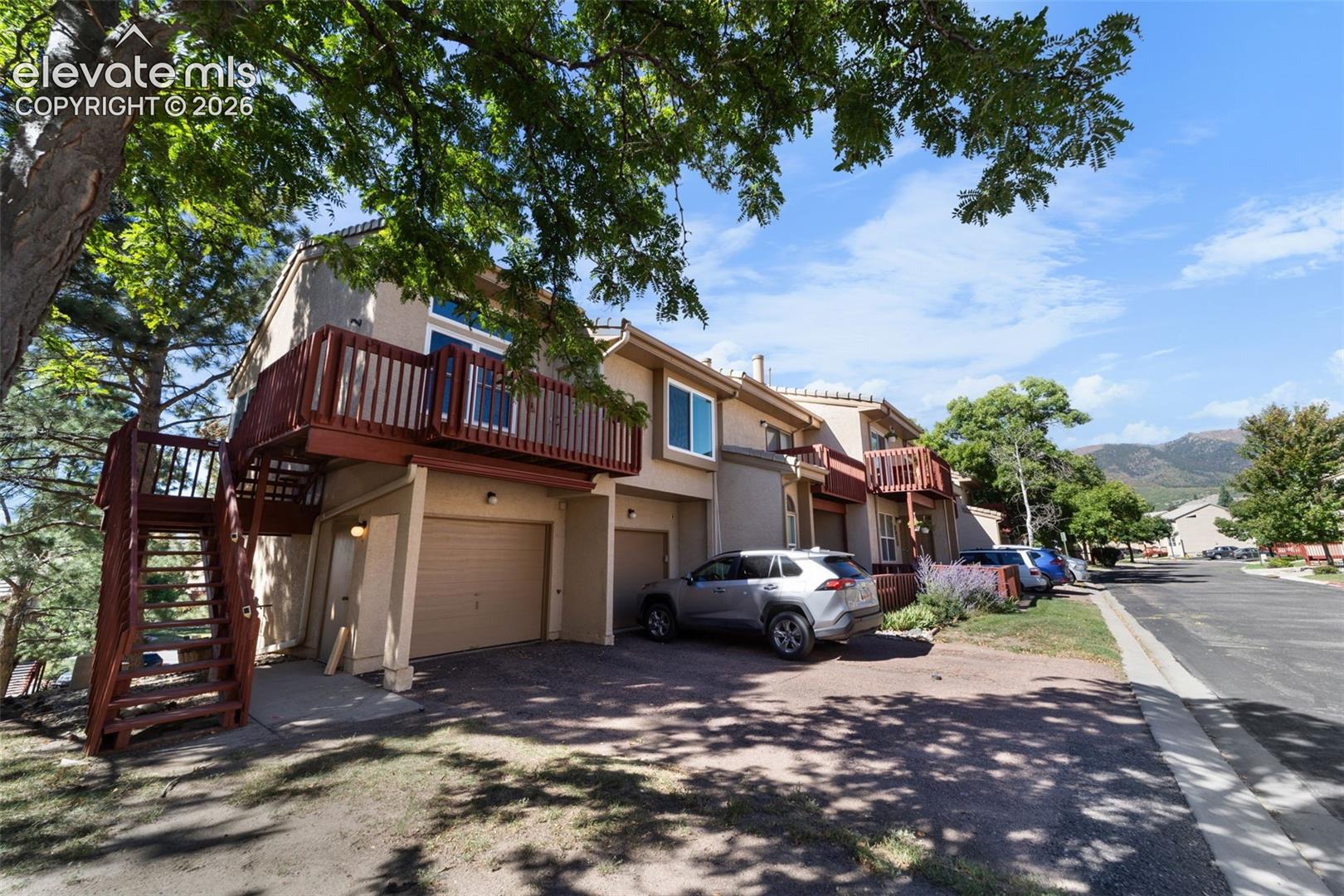 Multi-level exterior featuring wood-finish balcony, exterior staircase, concrete driveway, and attached garage