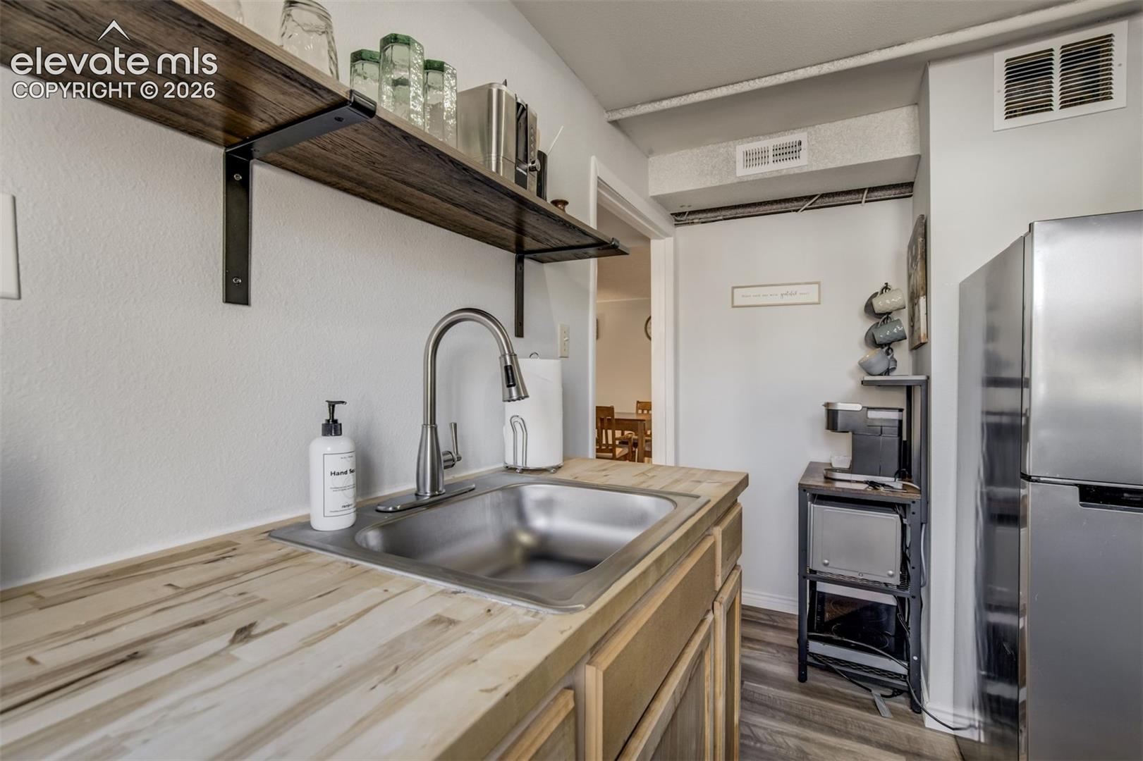 Stainless steel sink with a gooseneck faucet, light wood-finish countertops, wood-finish open shelving, and wood-finish lower cabinetry