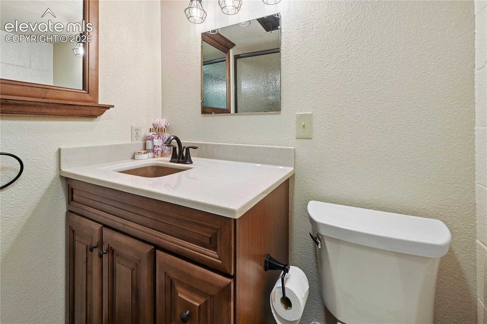 Wood-finish vanity with panel detailing, light-toned countertop, and bronze-finish faucet